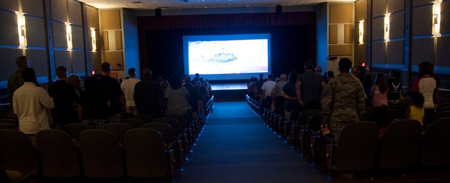 Movie theater attendees stand for The National Anthem Aug.  8, 2014, at Dyess Air Force Base, Texas. Although the movies are free, food and drinks must be purchased from the concession stand, which help offset the cost of up-keeping and maintaining of the theater, as well as the cost of the Navy Motion Picture Subscription, a service purchased through the Dyess Moral, Welfare and Recreation program. (U.S. Air Force photo by Airman 1st Class Kylsee Wisseman/Released)