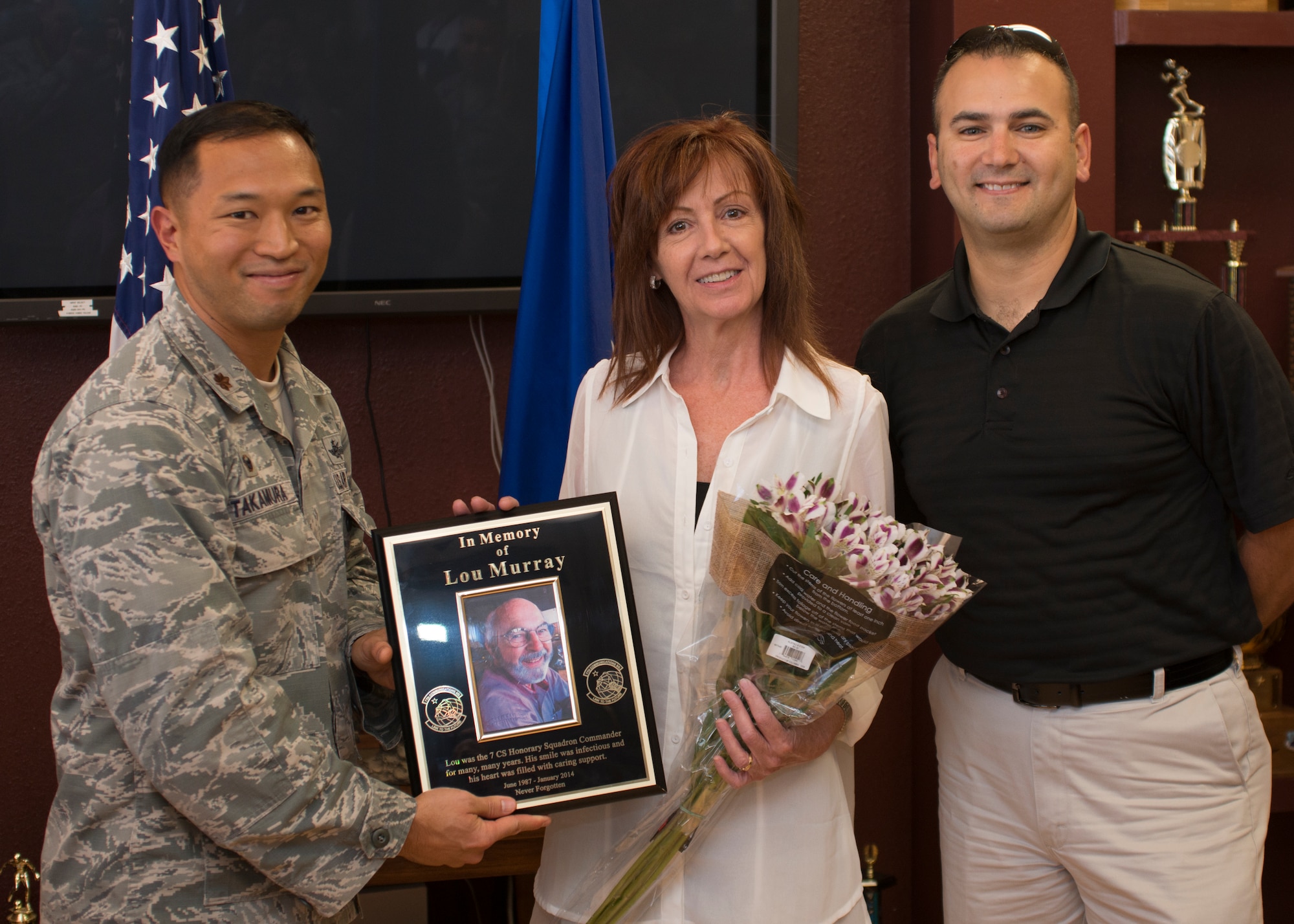 Mrs. Rhonna Murray, wife of the late Lou Murray, 7th Communication Squadron honorary commander, accepts a plaque and flowers from Maj. Kyle Takamura, 7th CS commander, and Lt. Col. Robert Mammenga, former 7 CS commander, during a ceremony commemorating Lou’s service and contributions to the unit August 7, 2014, at Dyess Air Force Base, Texas. Lou Murray served as the honorary commander for the 7th CS for 27 years. Before Lou became ill he would often participate in unit events or visit the squadron simply to give out treats and speak with the Airmen. He was always smiling. By understanding the operations tempo and functions of the Airmen assigned here, honorary commanders are able to communicate those stories of mission impact to a broader audience in the various community circles in which they operate. A plaque honoring Lou will permanently reside in the squadron’s heritage room. (U.S. Air Force photo by Senior Airman Peter Thompson/Released)