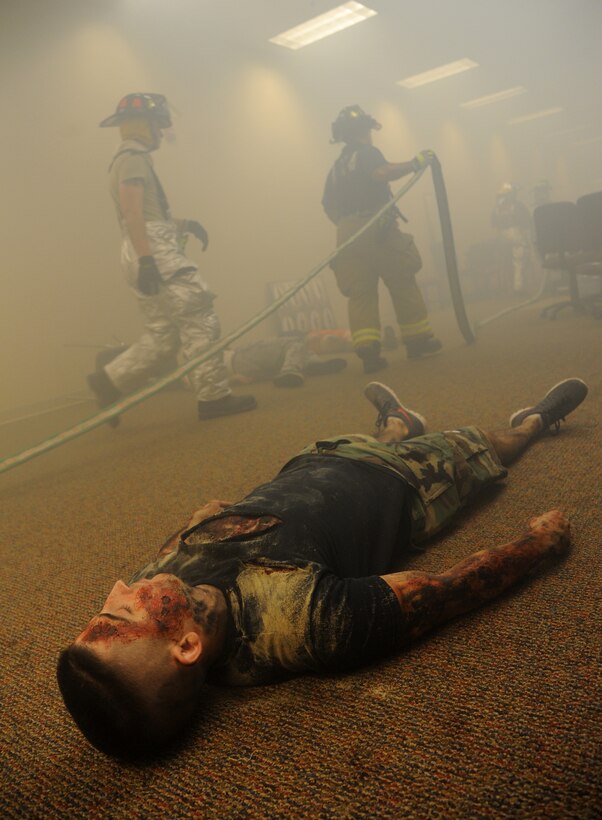 Tech. Sgt. Keith Brown, 338th Training Squadron, portrays a fire “victim,” as Staff Sgt. John Hood and Jerame Bullard, Keesler firefighters, drag a water hose into the simulated burning building as they search for the fire during a major accident response exercise Aug. 7, 2014, at the Locker House at Keesler Air Force Base, Miss. Team Keesler practiced real-world training during the exercise which simulated a gas line explosion that set a building on fire. Due to the extreme temperatures, exercise “players” wore minimal fire gear.  (U.S. Air Force photo by Kemberly Groue)