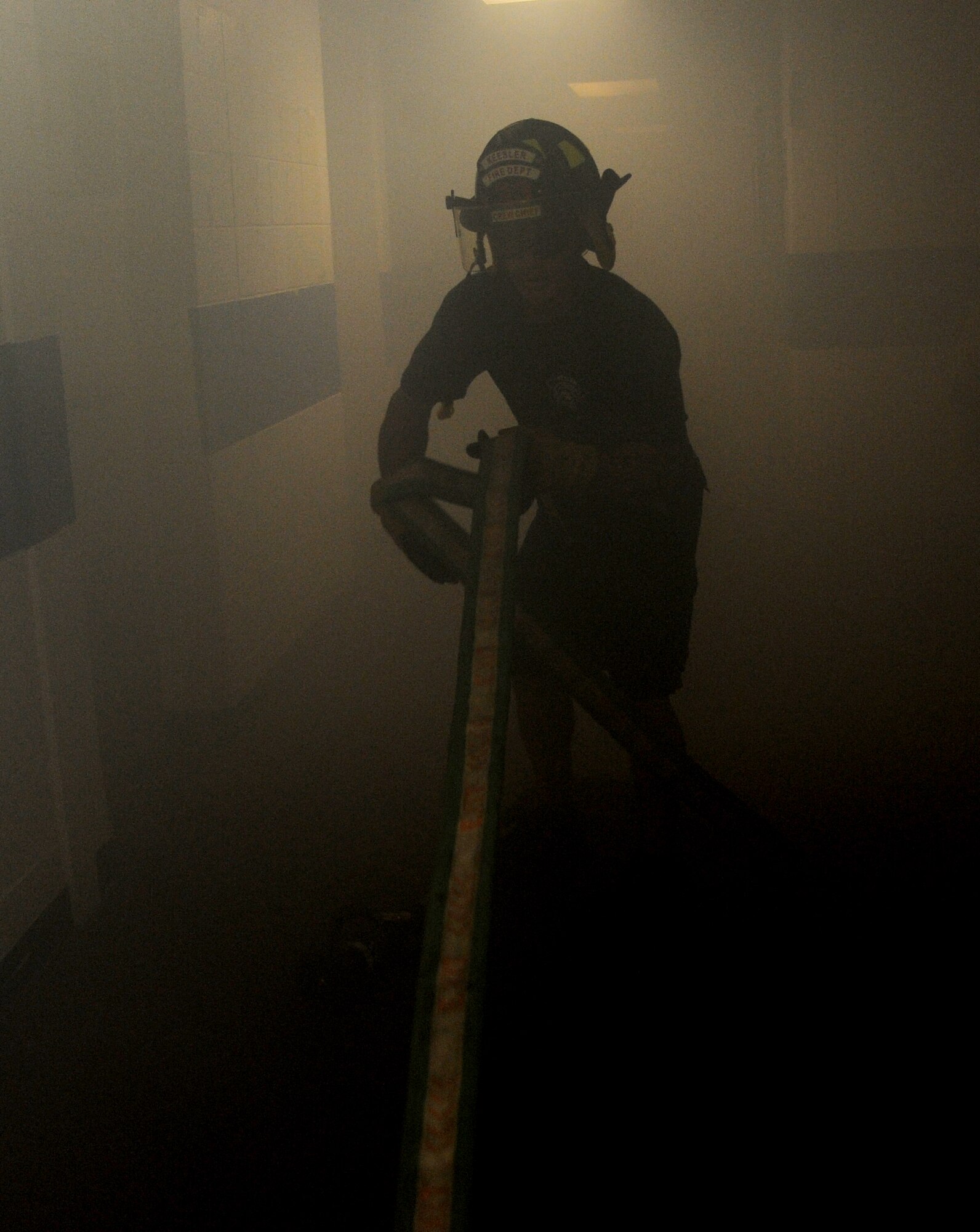 Raymond Bell, Keesler firefighter, pulls a water hose into the simulated burning building during a major accident response exercise Aug. 7, 2014, at the Locker House at Keesler Air Force Base, Miss. Team Keesler practiced real-world training during the exercise which simulated a gas line explosion that set a building on fire. Due to the extreme temperatures, exercise “players” wore minimal fire gear.  (U.S. Air Force photo by Kemberly Groue)
