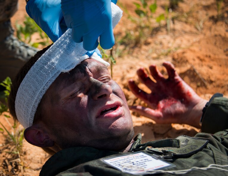 Master Sgt. Michael Sims, 5th Special Operations Squadron, has gauze secured to a head wound by 96th Medical Group Airman during a major accident response exercise Aug. 6 at Duke Field.  The simulated accident was a mid-air collision of a 33rd Fighter Wing joint strike fighter and a 919th Special Operations Wing C-145. Emergency responders from the base and the city were called to a downed aircraft scenario featuring fire, wreckage and victims with multiple injuries. The responders had to work as a team and coordinate movements at the simulated crash site, put out fires and attend to the wounded victims. (U.S. Air Force photo/Tech. Sgt. Jasmin Taylor)