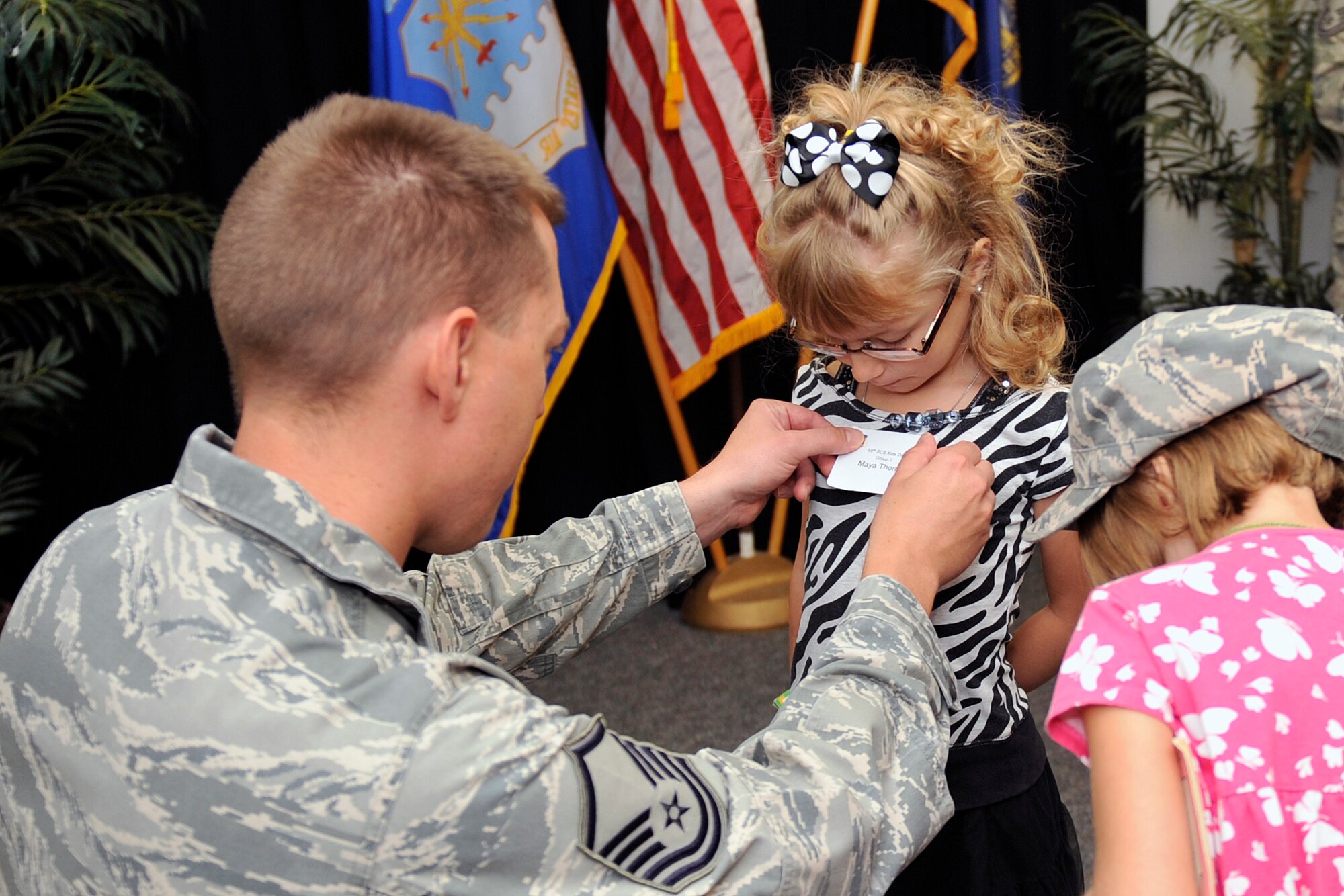 U.S. Air Force Master Sgt. Dustin Thorne, 55th Strategic Communication Squadron, gives his daughter, Maya, a name tag as she enters the 55th Communications Group building Aug. 7 as part of a Bring Your Child to Work event. Kids were given a mission briefing followed by a two-hour tour with their parents. (U.S. Air Force photo by Jeff W. Gates/Released)
