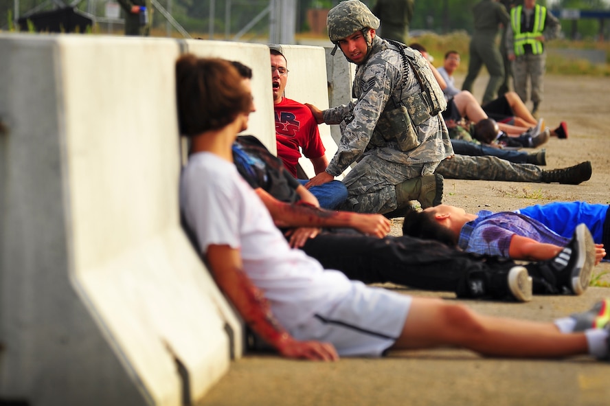 Staff Sgt. Sergio Hernandez, 5th Security Forces Squadron military working dog handler, tends to simulated wounded victims during an exercise on Minot Air Force Base, N.D., Aug. 5, 2014. The purpose of the exercise was to evaluate and validate the integration and response of emergency management, security forces, fire department, bioenvironmental and medical response members in a simulated radiological terrorist incident on Minot AFB. (U.S. Air Force photo/Senior Airman Brittany Y. Bateman)