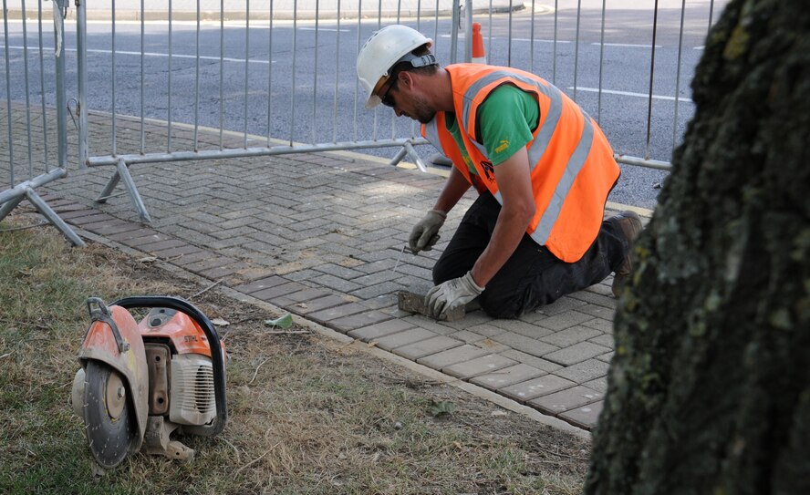 Matthew Bateson, a contractor from Kings Lynn, Norfolk, uses a trowel to mark a line on a paving brick Aug. 7, 2014, on RAF Mildenhall, England. Bateson replaced uneven bricks on the sidewalk near the base chapel to ensure the safety of pedestrians. (U.S. Air Force photo/Gina Randall/Released)