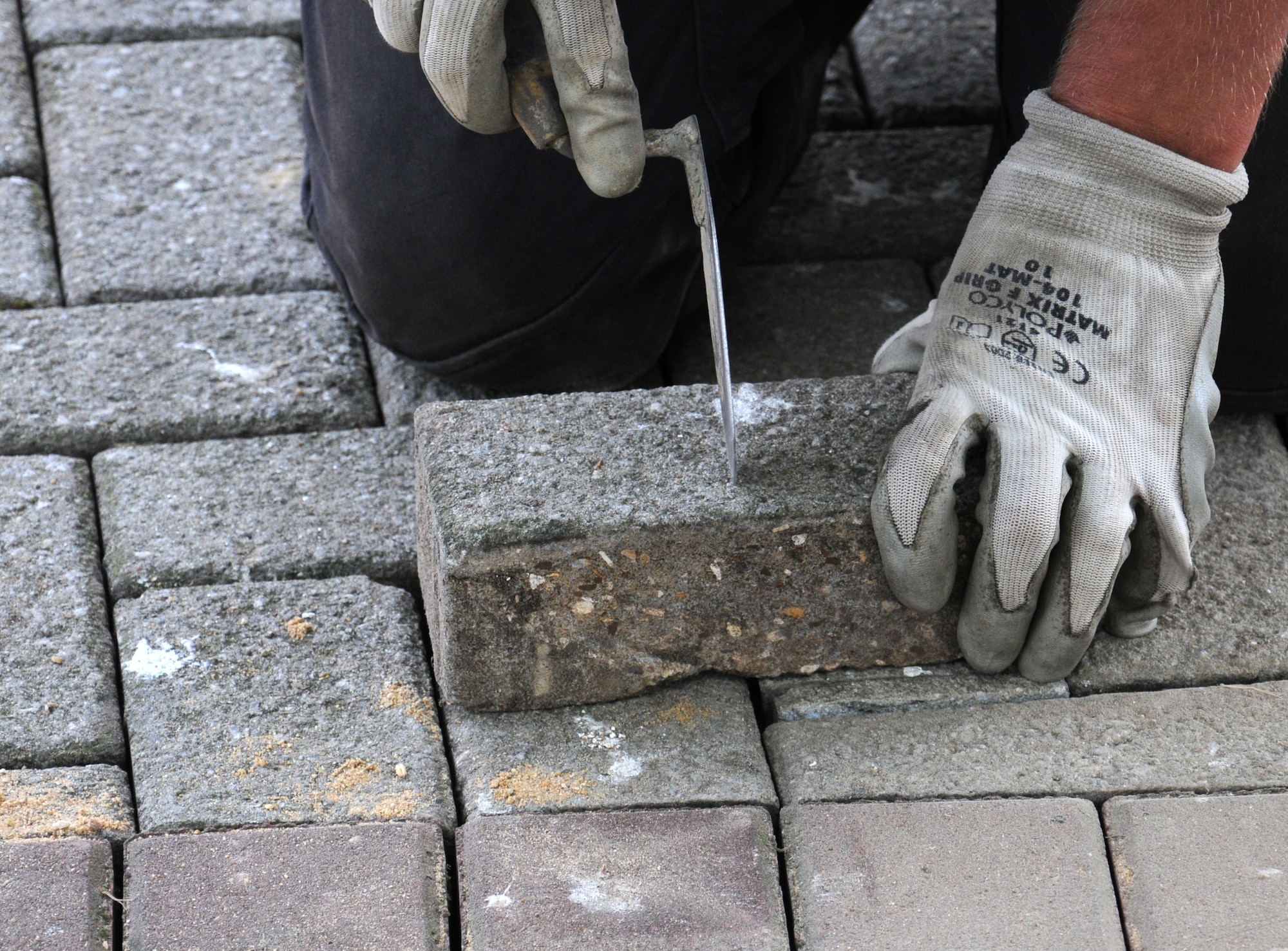 Matthew Bateson, a contractor from Kings Lynn, Norfolk, uses a trowel to mark a line on a paving brick Aug. 7, 2014, on RAF Mildenhall, England. Bateson then used a grind saw to cut the brick to the exact size to fit in the gaps in the brickwork. (U.S. Air Force photo/Gina Randall/Released)