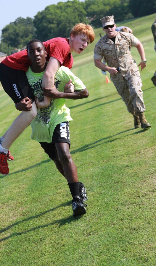 (Right) U.S. Marine Corps Staff Sgt. Isaac C. Acosta, Staff Non Commissioned Officer In Charge, Recruiting Sub Station Denton, encourages an Ardmore High School football player conducting a fireman’s carry on a teammate at Ardmore High School, OK, Aug. 4, 2014. The CFT is designed to be functional combat fitness training for deployed Marines. (U.S. Marine Corps photo by Sgt. Alfredo V. Ferrer)