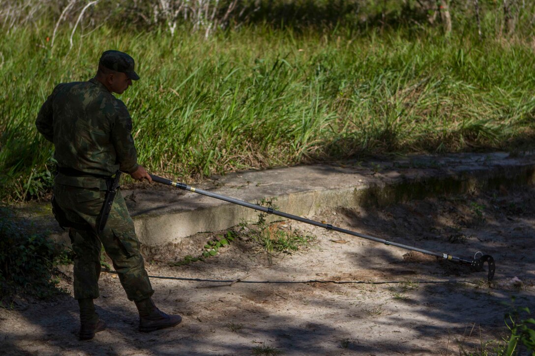 A Brazilian special forces Marine utilizes a holly stick to inspect the ground where a simulated improvised explosive device is suspected to be laid during a counter IED course held on Marambaia Island, Brazil, Aug. 6, 2014. The counter IED course was conducted by U.S. and Brazilian Marines in conjunction with a combat tracking course as part of a theater security cooperation bi-lateral exchange. Through close cooperation, the U.S. and its partners are ready to address transnational security challenges through integrated and coordinated approaches. SPMAGTF-South is currently embarked aboard the future amphibious assault ship USS America (LHA 6) in support of her maiden transit, "America Visits the Americas." (U.S. Marine Corps Photo by Cpl. Donald Holbert/ Released)