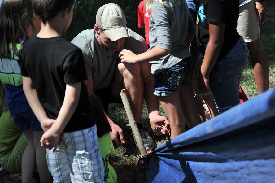 Senior Airman Troy Koontz teaches children from the Fairchild Air Force Base Youth Center how to build shelter in the wilderness at Clear Lake, Washington, Aug. 6, 2014. Koontz is a member of the 22nd Training Squadron.  Children from age’s five to 12 were given the opportunity to work on several exercises to teach them how to procure water, fire safety, and navigation and camouflage. (U.S. Air Force photo by Staff Sgt. Alexandre Montes/Released)