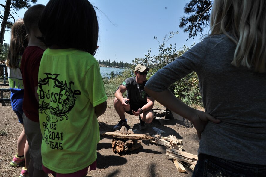 Senior Airman Trent Gareis talks to children from the Fairchild Air Force Base Youth Center about how to build camp fires and safety at Clear Lake, Washington, Aug. 6, 2014. Gareis is a member of the 22nd Training Squadron. Children from age’s five to 12 were given the opportunity to work on several exercises to teach them how to procure water, fire safety, and navigation and camouflage. (U.S. Air Force photo by Staff Sgt. Alexandre Montes/Released)