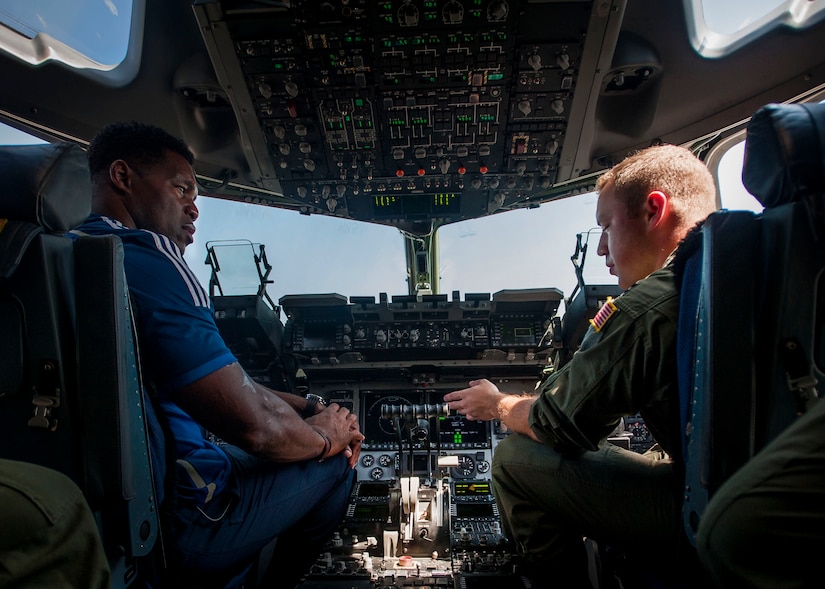 Herschel Walker, former NFL running back and Heisman Trophy winner, listens to Capt. Gerald Coscarelli, 16th Airlift Squadron C-17 pilot, as he explains what the C-17 Globemaster III brings to the warfighter Aug. 6. 2014, at Joint Base Charleston
, S.C. Walker visited the base to share his story about growing up in Georgia, playing professional football and how he sought help from mental health professionals for his struggles with dissociative identity disorder. Walker spoke and met Sailors and Airmen at both the Weapons Station and Air Base where he met with service members and their families and signed autographs. Walker played college football at the University of Georgia and spent 14 years  in the NFL.  (U.S. Air Force Photo / Senior Airman Tom Brading)
