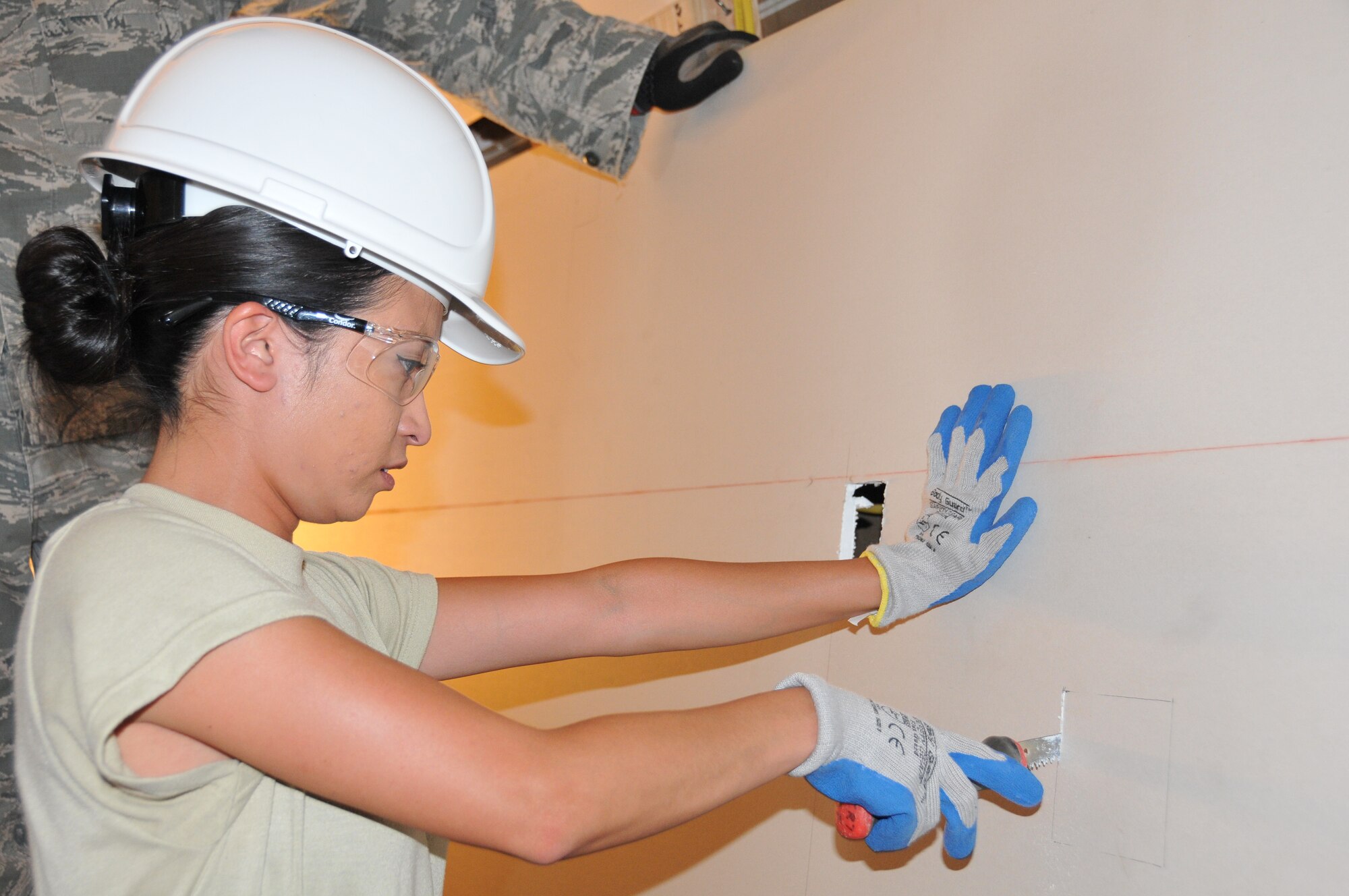 Airman Katrina Gambo, a 512th Civil Engineer Squadron electrician, cuts out a portion of dry wall to accommodate an electrical outlet in a module home being built in Gallup, N.M., July 21, 2014. Homes are built in a warehouse and transported to a Navajo reservation as part of the Department of Defense's Innovative Readiness Program, which provides Air Force reservists with real world experience. (U.S. Air Force photo/Staff Sgt. Mercedes Crossland)