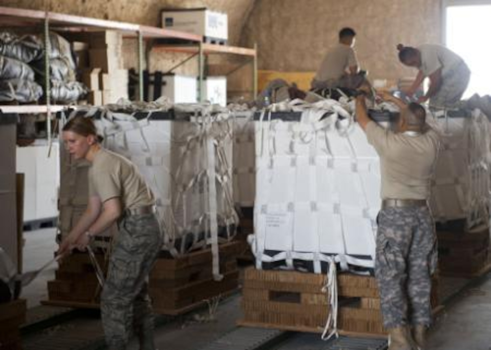 Service member volunteers push a completed pallet of food and water to prepare it for loading onto aircraft at a location in Southwest Asia Aug. 11, 2014. Volunteers from across the base came out to help build pallets of humanitarian aid. The pallets are being airdropped to displaced citizens in the vicinity of Sinjar, Iraq. (U.S. Air Force photo by Senior Airman Colin Cates)







