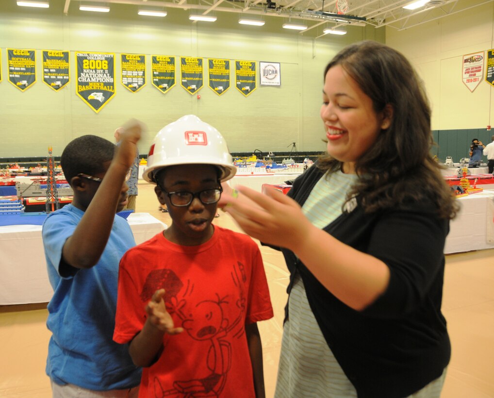 Civil Engineer Zaniah Andino, U.S. Army Corps of Engineers, Baltimore District, places a construction hat on an attendee at the TEACH FLEET Lego Show and STEM Expo on Aug. 8.  Andino volunteered to take part in the event and spoke with many of the children in attendance about her career as a Corps employee.  She also facilitated a break-out session at the Show and Expo, where children and their families had the opportunity to use the West Point Bridge Building Software.  