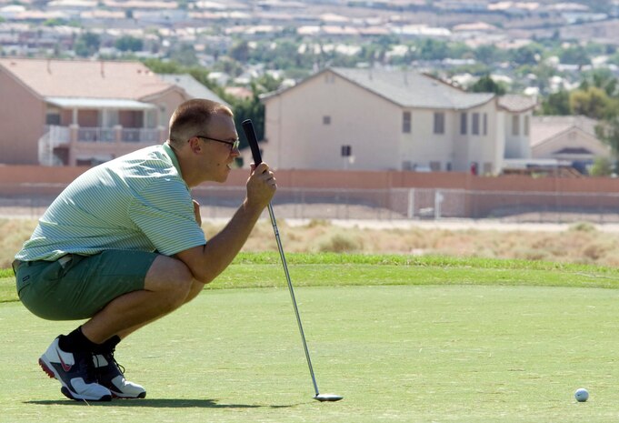 Senior Airman Nathen Hopkins, 57th Aircraft Maintenance Squadron F-35 Lightning mechanic, crouches down to estimate how far the ball needs to go to get in the sixth hole  during the 2014 intramural golf championship at Nellis Air Force Base, Nev., Aug. 12, 2014. Hopkins and the 57th AMXS, won the championship in 2013, and were defeated by the 99th Civil Engineer Squadron during this year’s championship match. (U.S. Air Force photo by Airman 1st Class Rachel Loftis)