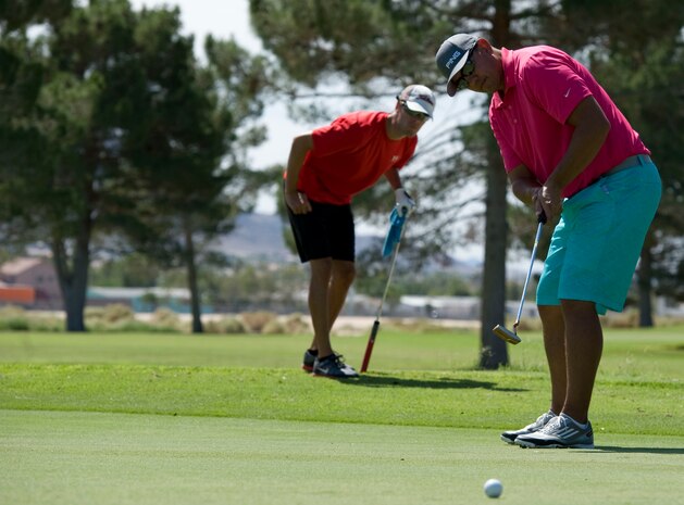 Master Sgt. Alex Ackley, (front) 99th Civil Engineer Squadron real property manager, putts a golf ball on the eighth hole during the 2014 intramural golf championship at Nellis Air Force Base, Nev., Aug. 12, 2014. The 99th CES golf team defeated the 57th Aircraft Maintenance Squadron to claim the championship for 2014. (U.S. Air Force photo by Airman 1st Class Mikaley Towle)