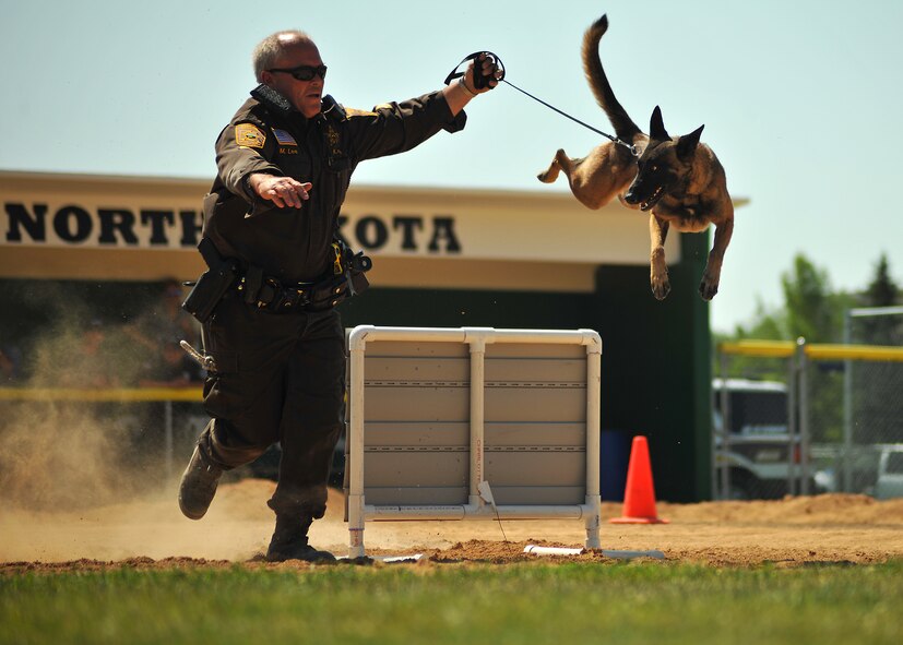 Cpl. Mike Lee, Grand Forks County Sheriff’s Department K9 handler, runs alongside Sheeba as she jumps over a wall hurdle during the Iron Dog Course at Apollo Park on Aug. 13, 2014, in the city of Grand Forks, N.D. The event is part of the North Dakota Peace Officers Association’s K9 Challenge, which features explosives and narcotics detection; patrol maneuvers and an iron dog course. (U.S. Air Force photo/Senior Airman Xavier Navarro)