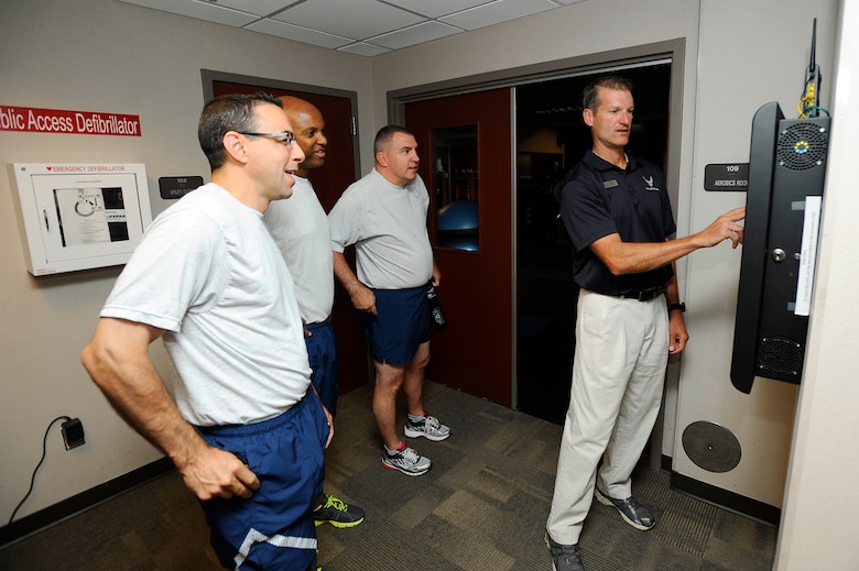 Col. Bill Liquori, 50th Space Wing commander, and the rest of the wing leadership, receive step-by-step instructions on how to use the new fitness center kiosk from Seth Cannello, base fitness and sports manager, Aug. 11, 2014, at Schriever Air Force Base, Colo. The on-demand fitness kiosk features various classes, such as aerobics, Pilates, yoga and spinning. (U.S. Air Force photo/Christopher DeWitt)