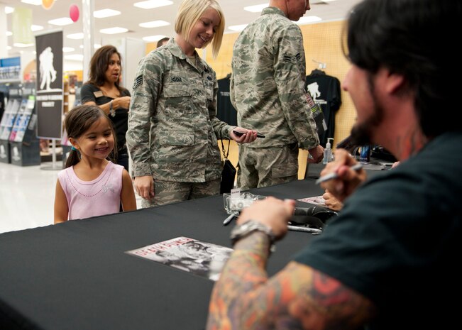 Kalena, daughter of Staff Sgt. Nicole Igoa, U.S. Air Force Warfare Center judge advocate paralegal, receives an autograph from Jason Hook , heavy metal band Five Finger Death Punch lead guitarist at the Exchange at Nellis Air Force Base, Nev., Aug. 11, 2014. Kalena was one of many fans who lined up at the Main Exchange for the chance to meet and get autographs from the band. (U.S. Air Force photo by Airman 1st Class Thomas Spangler)