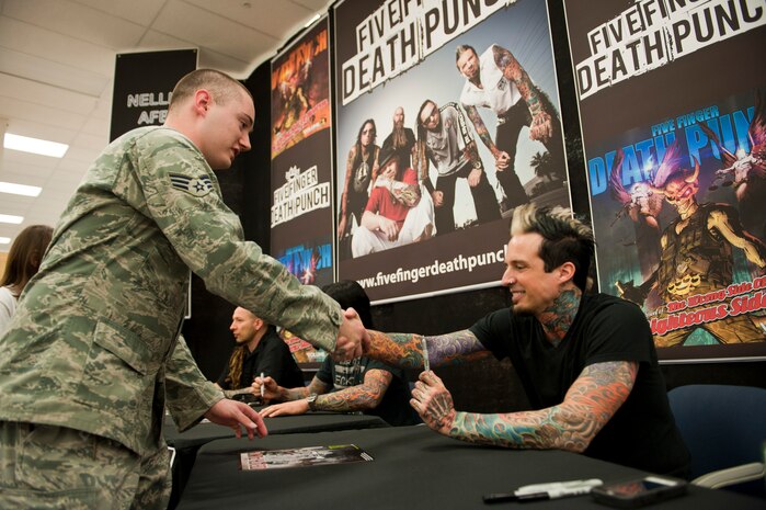 Senior Airman Dylan Johnson, 99th Force Support Squadron career development counselor, shakes hands with Jeremy Spencer , heavy metal band Five Finger Death Punch drummer at the Exchange at Nellis Air Force Base, Nev., Aug. 11, 2014. The band signed autographs and debuted a music video which focused on the many challenges that veterans face, such as post-traumatic stress disorder and homelessness. (U.S. Air Force photo by Airman 1st Class Thomas Spangler)