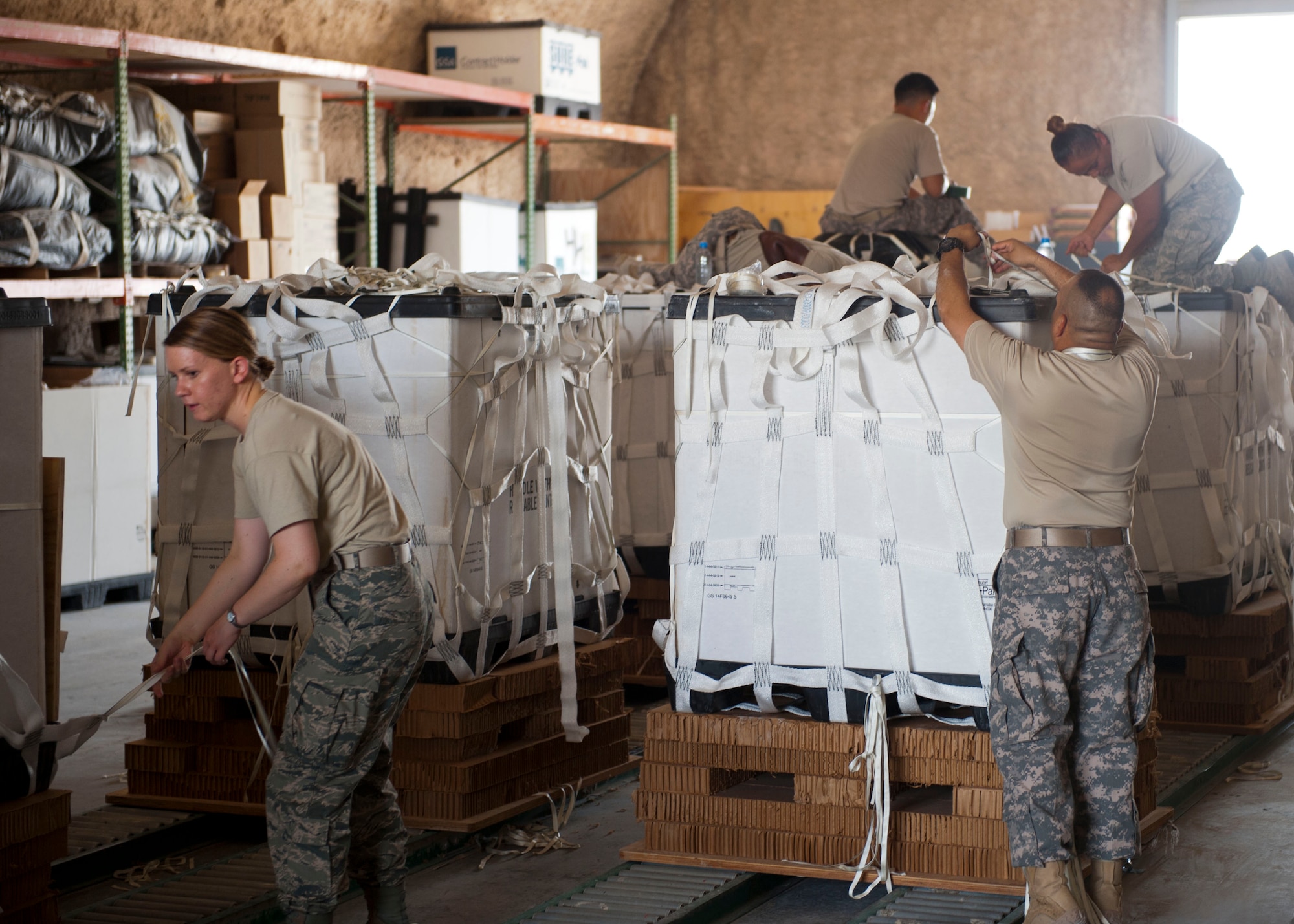 Service member volunteers push a completed pallet of food and water to prepare it for loading onto aircraft at a location in Southwest Asia Aug. 11, 2014. Volunteers from across the base came out to help build pallets of humanitarian aid. The pallets are being airdropped to displaced citizens in the vicinity of Sinjar, Iraq. (U.S. Air Force photo by Senior Airman Colin Cates)