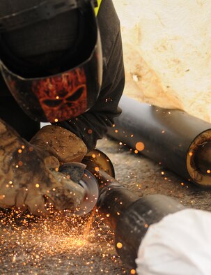 Duncan Steele, a contractor from North Hampshire, England, grinds a pipe to smooth it out after welding Aug. 8, 2014, on RAF Mildenhall, England. The pipes will be used for a heating system that will replace the outdated system near the 100th Air Refueling Wing command post. (U.S. Air Force photo/Airman 1st Class Jonathan Light/Released)