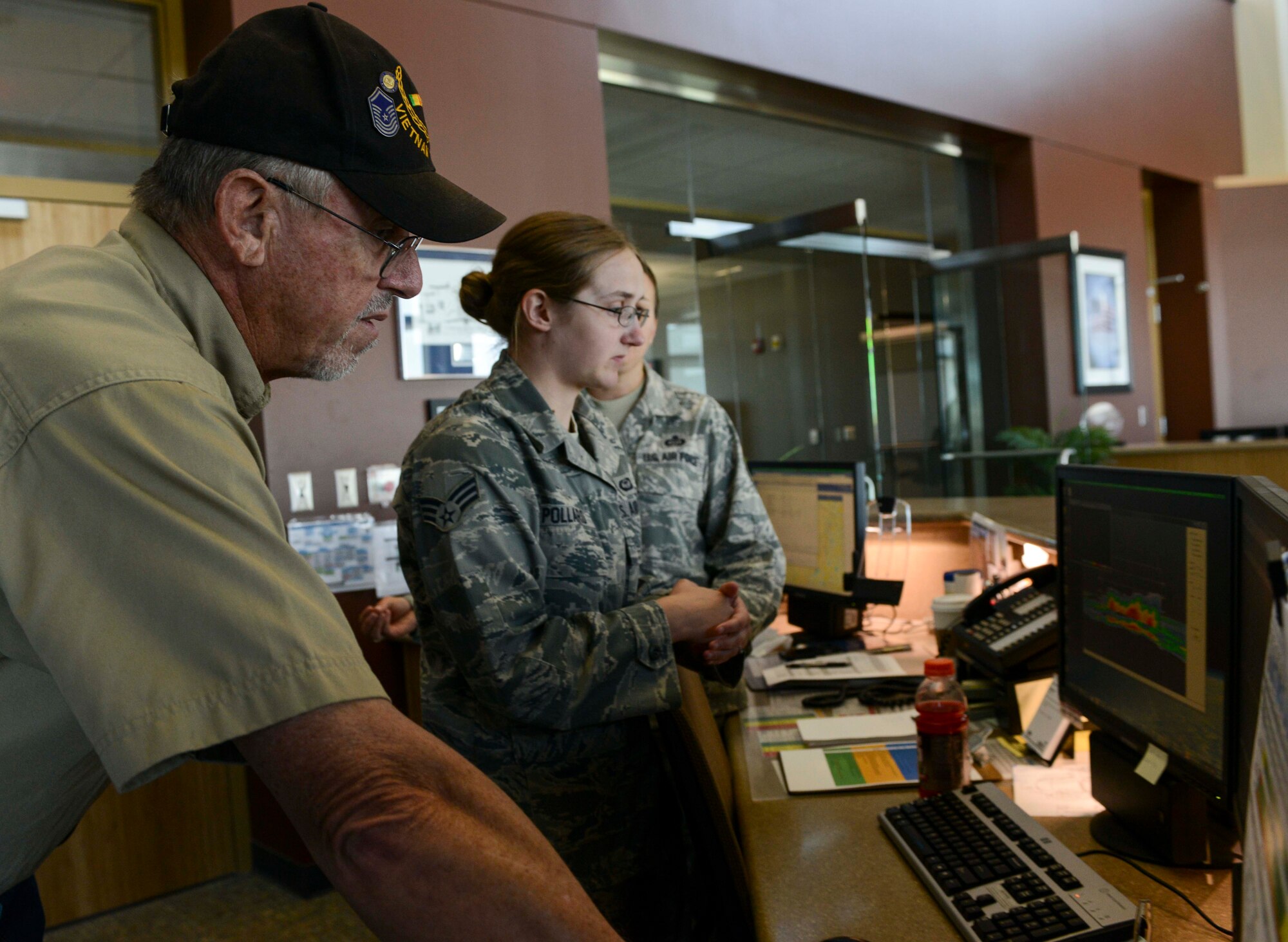 Retired Senior Master Sgt. Dennis Miller is shown weather radar software by Senior Airman Samantha Pollard, 5th Operations Squadron weather forecaster, on Minot Air Force Base, N.D., Aug. 8, 2014. During his career, Miller was a key member of a team that installed a CPS9 long-pause weather radar in Nakhon Phanom, Thailand, to monitor the weather over Hanoi during the Vietnam War. (U.S. Air Force photo/Senior Airman Stephanie Morris.)