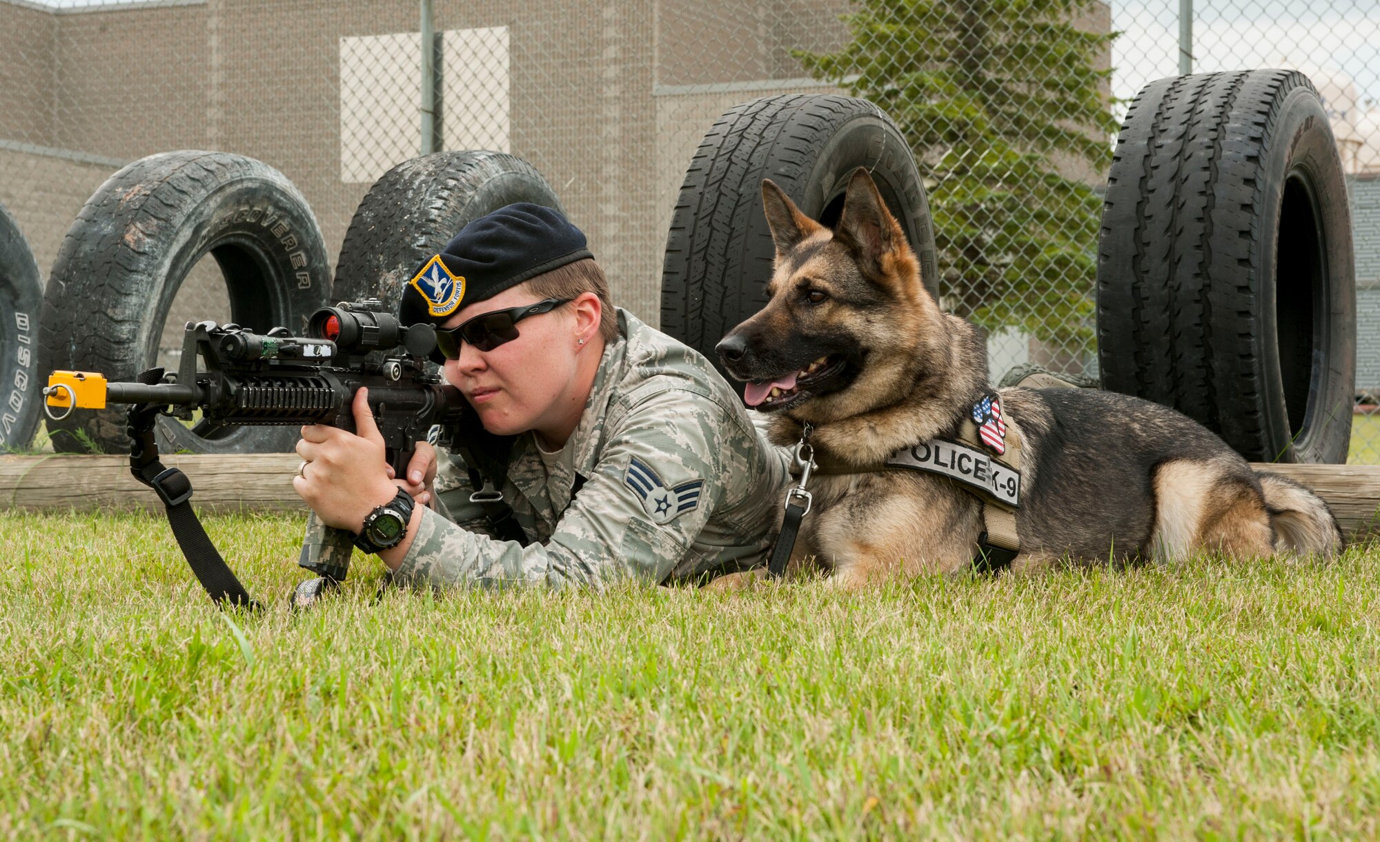 Senior Airman Heather Johnson, 5th Security Forces Squadron military working dog handler, fires blanks during weapons training as her MWD Cyndy lies next to her on Minot Air Force Base, N.D., July 29, 2014. This training allows handlers to familiarize their dogs with the sound of gun fire and gauge what their reaction will be in a combat situation. (U.S. Air Force photo/Senior Airman Stephanie Morris)