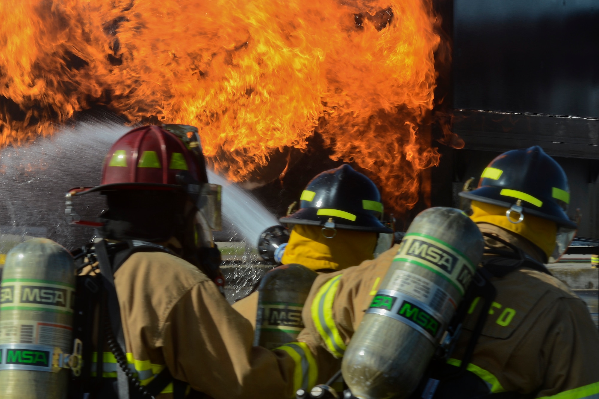 Firefighters of the 48th Civil Engineer Squadron Fire Department spray a mock F-15 with water during live fire training at the burn pit on Royal Air Force Lakenheath, England, Aug. 13, 2014. All firefighters are required to conduct live fire training twice a year to avoid skill fade and keep their qualifications current. (U.S. Air Force photo by Airman 1st Class Trevor T. McBride/Released)