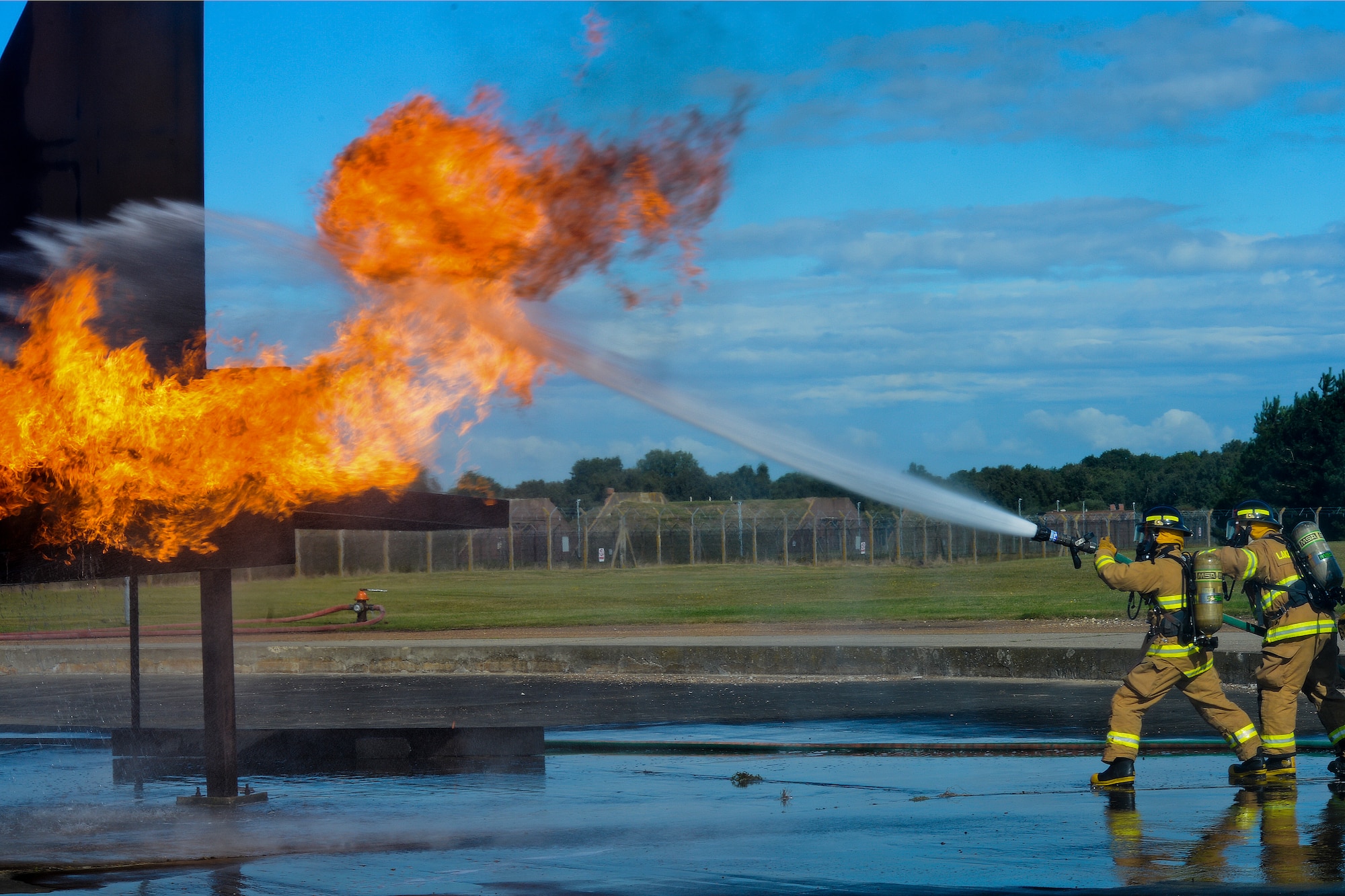 Firefighters of the 48th Civil Engineer Squadron Fire Department spray a mock F-15 engine with water during live fire training at the burn pit on Royal Air Force Lakenheath, England, Aug. 13, 2014. All firefighters are required to conduct live fire training twice a year to avoid skill fade and keep their qualifications current. (U.S. Air Force photo by Airman 1st Class Trevor T. McBride/Released)