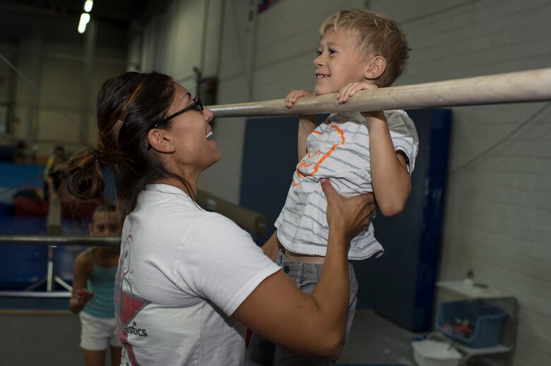 Cat Schnoes, gymnastics coach, wife of Tech. Sgt. Karl Schnoes, 52nd Civil Engineer Squadron firefighter, assists Logan Black, son of Jessica Black, to perform a pull-up during the Exceptional Family Member Program camp at Bitburg Annex, Germany, Aug. 12, 2014. The EFMP family support coordinator helps families identify and access programs and services for their child’s need. (U.S. Air Force photo by Staff Sgt. Christopher Ruano/Released)