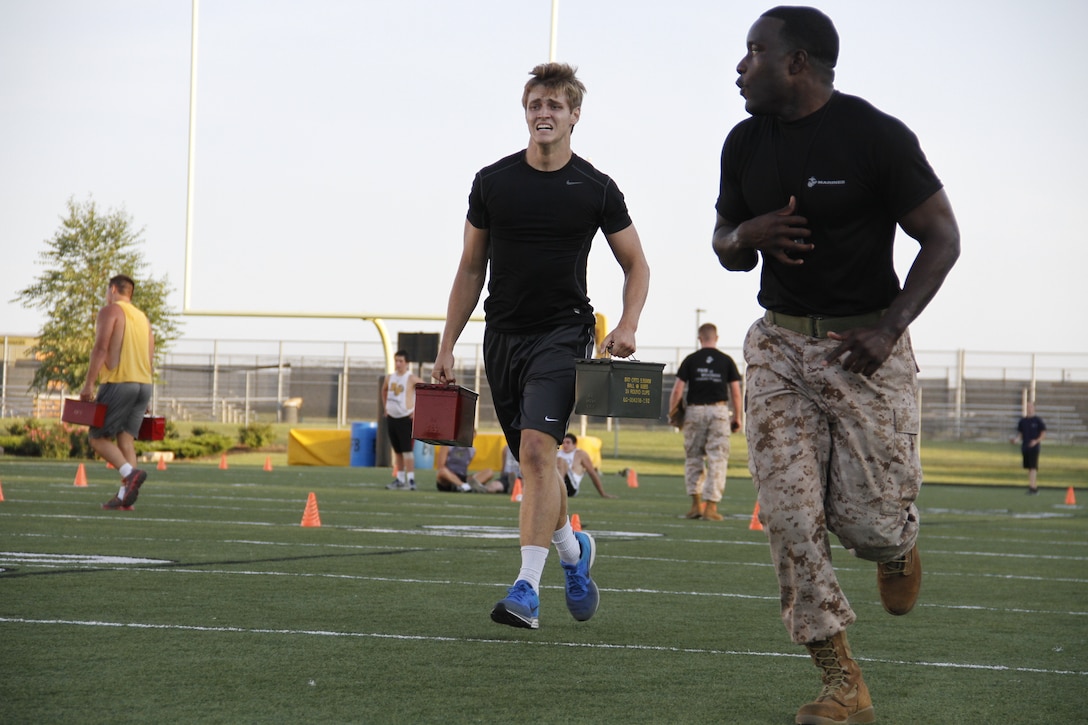 Beau A. Bequeaith, a senior Blue Valley High School Tigers tight end, grimaces as he sprints with two 30-pound ammunition cans as part of the Marine Corps Combat Fitness Test as Sgt. Laronald McKinney, a Marine Corps Recruiting Station Kansas City, Recruiting Sub-Station Olathe recruiter, sprints ahead to motivate Bequeaith to the end. The CFT is substantially different from a normal regiment of football and was seen as a way to shake up the usual routine pf practice before the season starts.