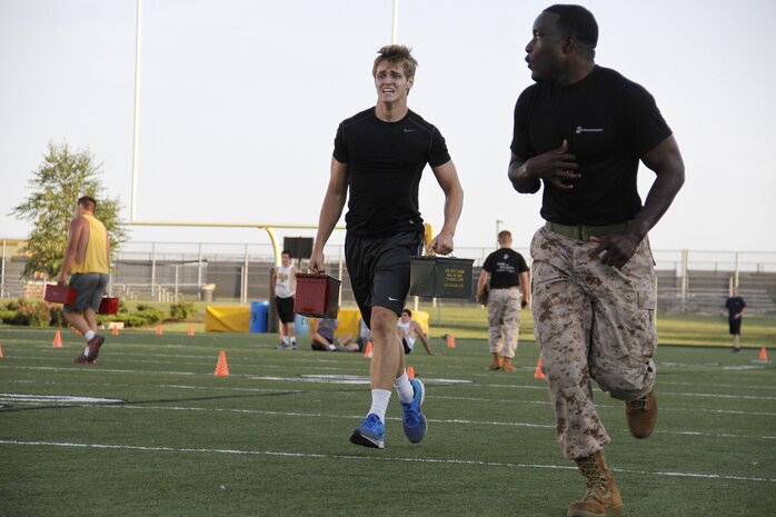 Beau A. Bequeaith, a senior Blue Valley High School Tigers tight end, grimaces as he sprints with two 30-pound ammunition cans as part of the Marine Corps Combat Fitness Test as Sgt. Laronald McKinney, a Marine Corps Recruiting Station Kansas City, Recruiting Sub-Station Olathe recruiter, sprints ahead to motivate Bequeaith to the end. The CFT is substantially different from a normal regiment of football and was seen as a way to shake up the usual routine pf practice before the season starts.