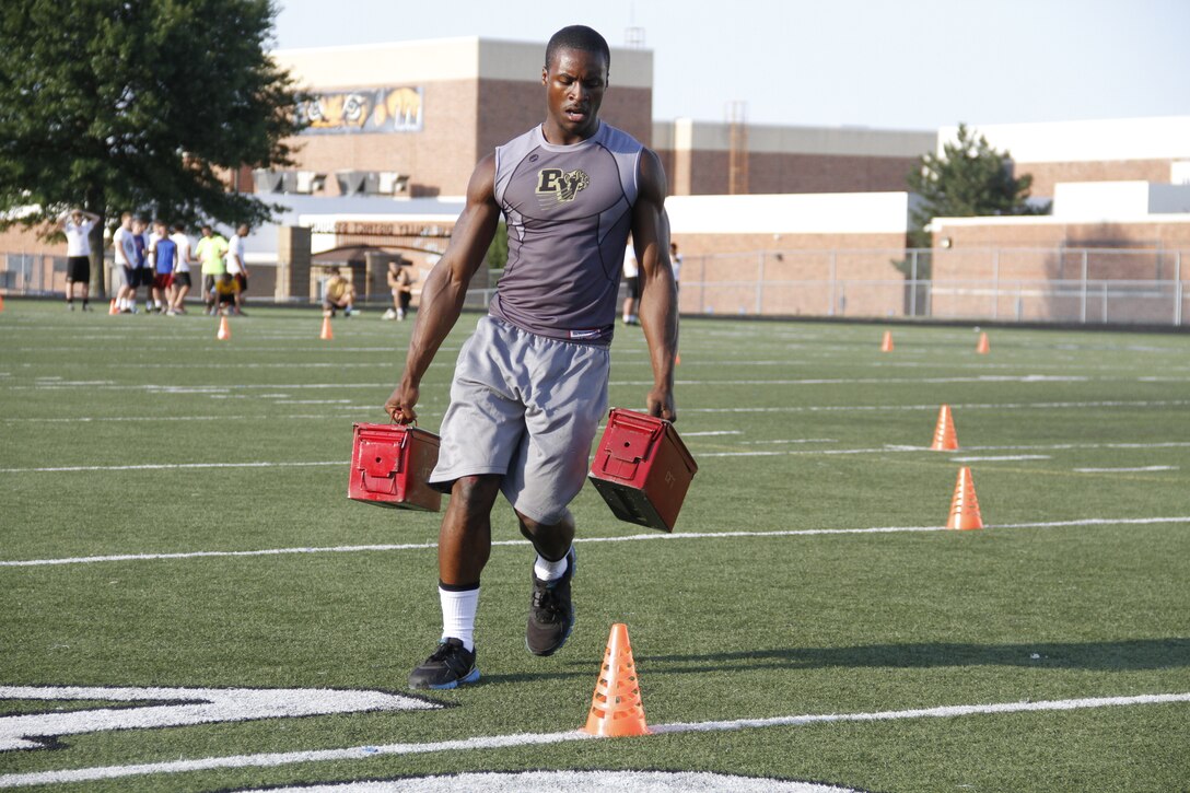 Gannon C. Cornley, a senior Blue Valley High School Tigers cornerback, running back, and wide receiver, performs cone drills while carrying two 30-pound ammunition cans during the Marine Corps' Combat Fitness Test at the Lamar District Athletic Complex Aug. 14, 2014. Marines from Recruiting Station Kansas City and Recruiting Sub-Station Olathe psuhed the players to dig deep and finish strong. The CFT consists of an 880-meter sprint, ammo-can lifts in two minutes, and a maneuver-under-fire portion.