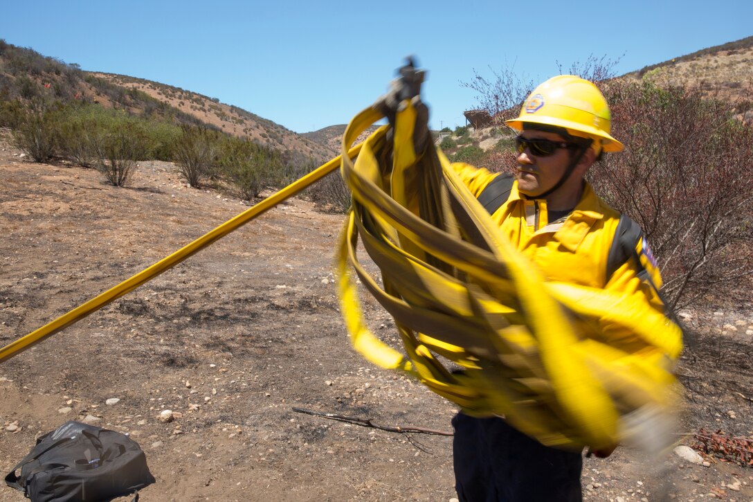 Brian Cato, a firefighter with the Miramar Fire Department, disassembles a rolled fire hose after the wildland firefighting exercise with 3rd Marine Aircraft Wing aviators aboard Marine Corps Air Station Miramar, Calif., Aug. 14. The training was designed to build a communication based foundation for firefighters and aviators to build on in case of future fires either aboard the air station or San Diego community.