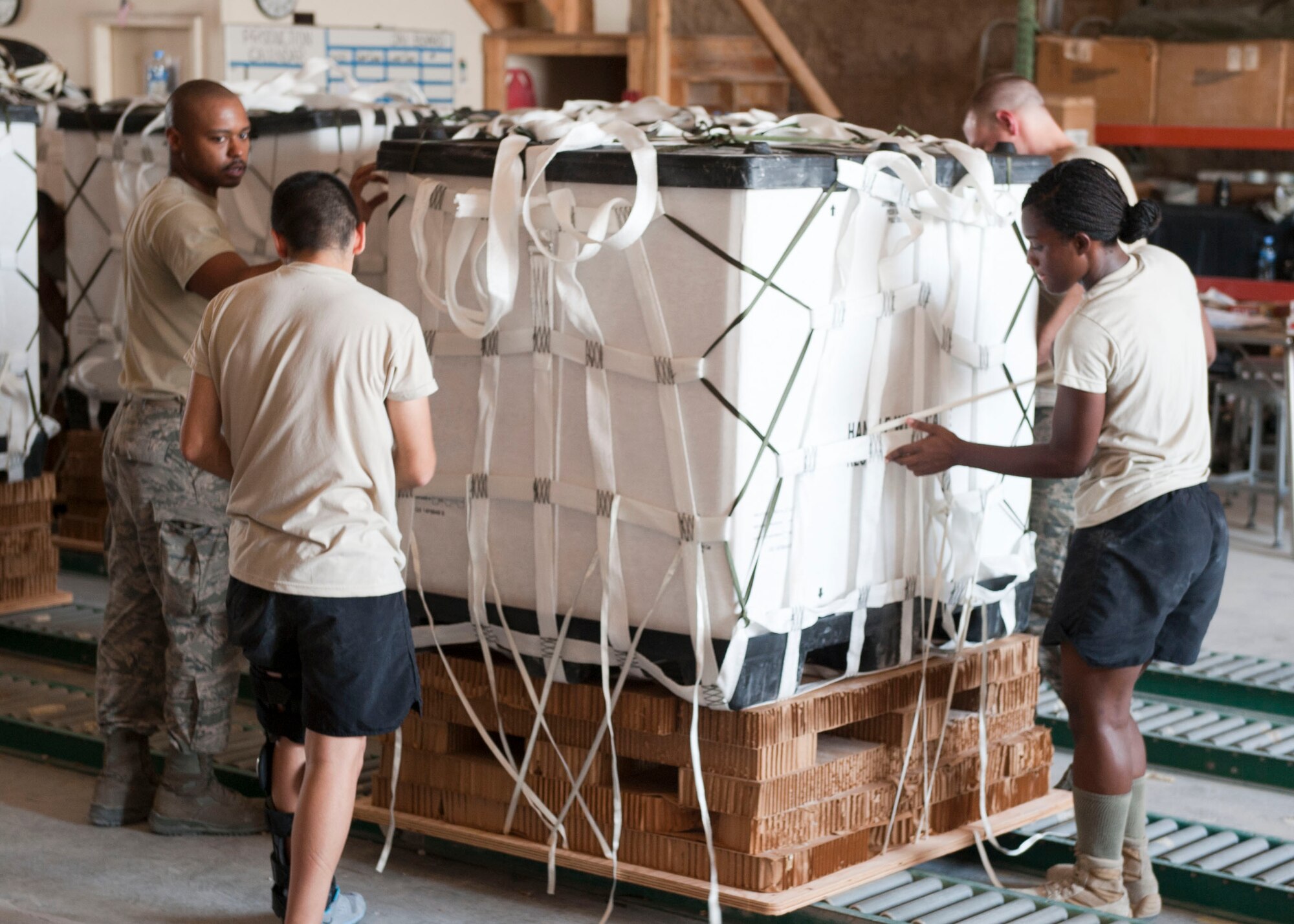 Service member completed a pallet of food and water to prepare it for loading onto aircraft at Al Udeid Air Base, Qatar, Aug. 13, 2014. Volunteers from across the base came out to help build pallets of humanitarian aid, they are completing on average over one hundred pallets a day. The pallets are being airdropped to displaced citizens in the vicinity of Sinjar, Iraq. (U.S. Air Force photo by Senior Airman Colin Cates) 