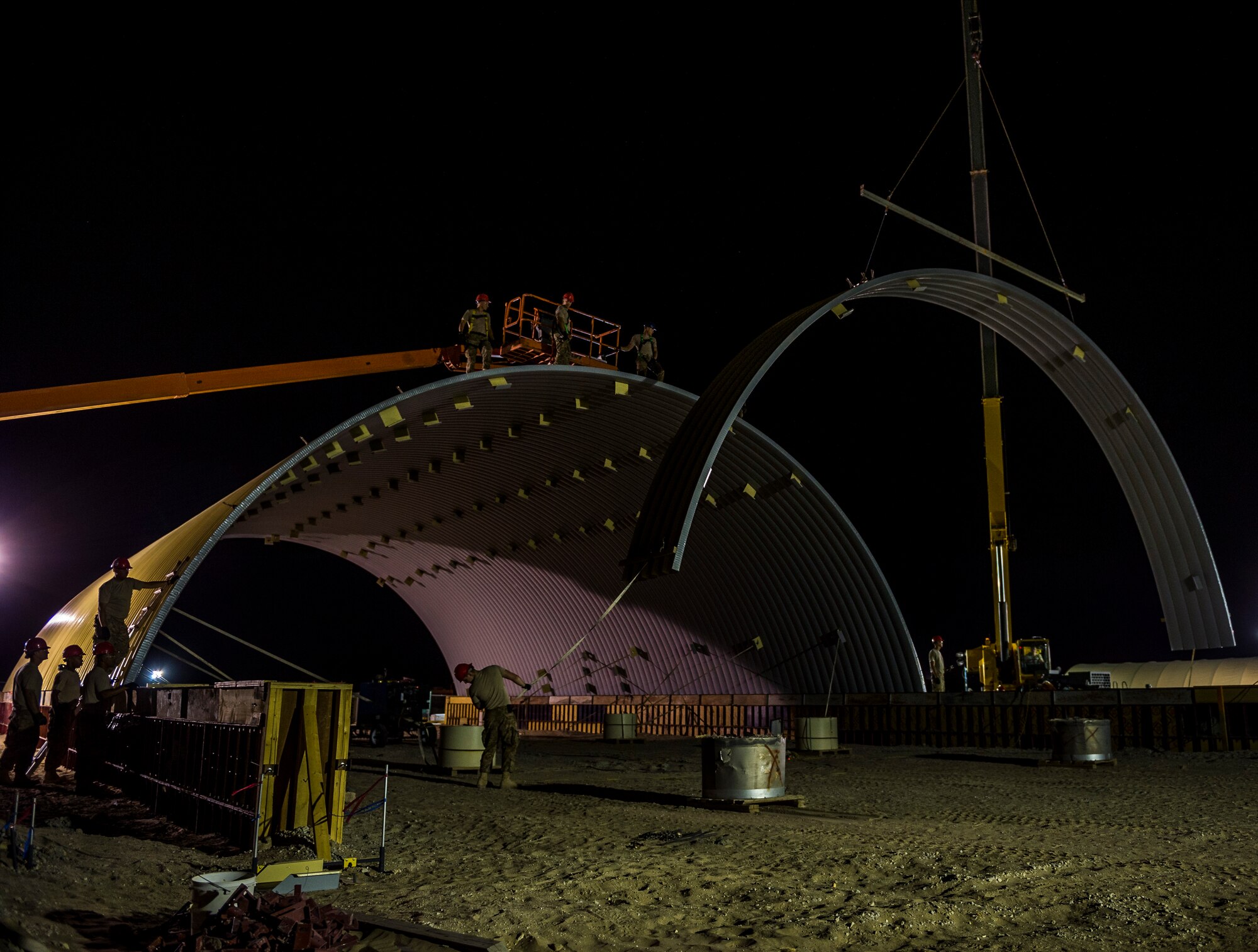 Airmen from the 557th Expeditionary RED HORSE Squadron use a crane to position steel arches for a K-Span building Aug. 4, 2014 at an undisclosed location in Southwest Asia. Airmen from the 557th ERHS came from Al Udeid to build two K-Span buildings to establish more permanent structures than the current tents used as passenger terminals. The unit is comprised of all Air National Guard members deployed from Penn. in support of Operation Enduring Freedom. (U.S. Air Force photo by Staff Sgt. Jeremy Bowcock)