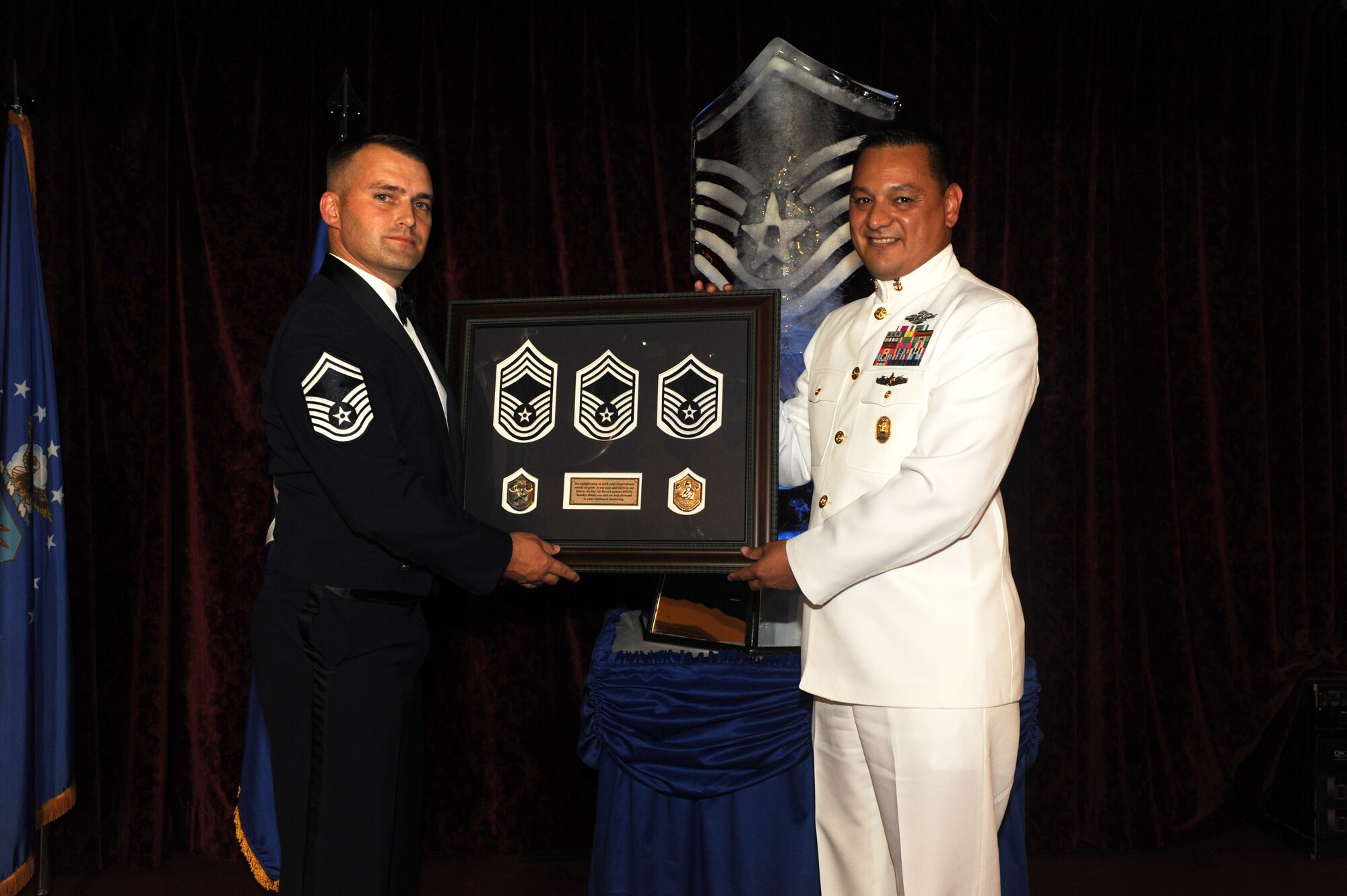 U.S. Navy Master Chief Petty Officer Alfredo Chavez, command master chief for 1st Marine Aircraft Wing, III Marine Expeditionary Force, is presented a gift from U.S. Air Force Senior Master Sgt. Stephen Griffieth, 18th Communications Squadron plans and rescources flight chief and Top 3 President, during the Senior NCO Induction ceremony on Kadena Air Base, Japan, Aug. 15, 2014. Chaves was the guest speaker for the event and spoke about what it means to be a leader and how to lead by example. The ceremony was a celebration for those who have been selected to put on the rank of master sergeant. (U.S. Air Force photo by Airman 1st Class Stephen G. Eigel/Released)