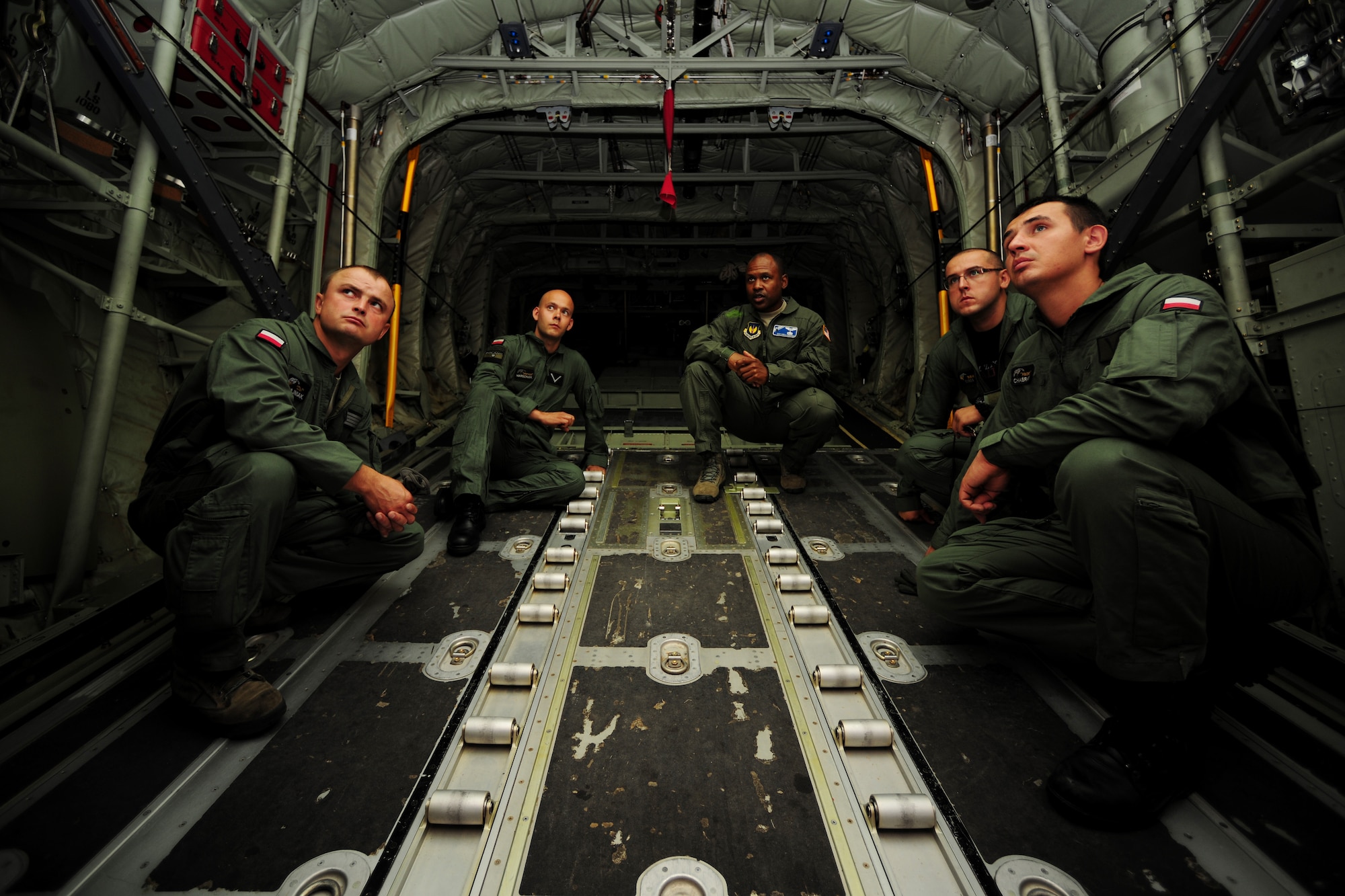 Master Sgt. Chris Minnifield, center right, discusses the finer points of C-130 Hercules mass container delivery airdrop operations with Polish air force service members Aug. 11, 2014, at Powidz Air Base, Poland. The bilateral training was to prepare Polish forces to conduct equipment and supply delivery missions to Iraq. Minnifield is a 37th Airlift Squadron loadmaster. (U.S. Air Force photo/Staff Sgt. Jarad A. Denton)