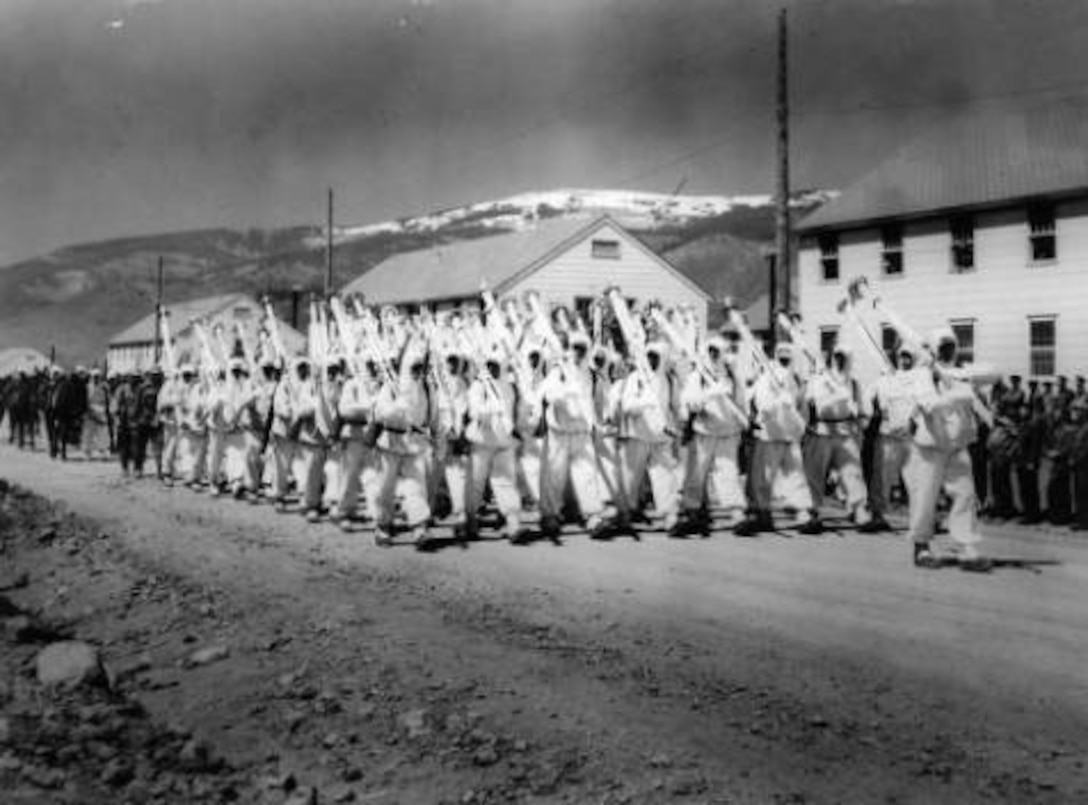 10th Mountain Division soldiers parade down a street at Camp Hale, Colo., probably in 1943. They are wearing their “whites” the winter camouflage uniforms and carry white skis on their right shoulder as rifles are normally carried while on parade. Photo part of the Western History Collection at the Denver Public Library.