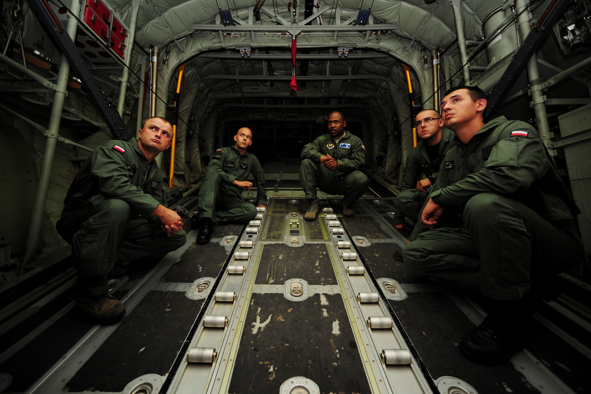 U.S. Air Force Master Sgt. Chris Minnifield, 37th Airlift Squadron loadmaster, center, discusses the finer points of C-130 mass container delivery airdrop operations with Polish Air Force Service members at Powidz Air Base, Poland, Aug. 11, 2014. The bilateral training was held in preparation for Polish forces to conduct equipment and supply delivery missions tor Iraq. (U.S. Air Force photo by Staff Sgt. Jarad A. Denton/Released)