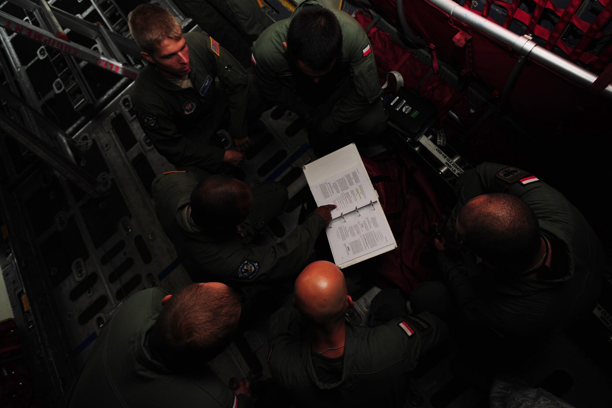 U.S. Air Force Master Sgt. Chris Minnifield, 37th Airlift Squadron loadmaster, center, reviews C-130E Hercules technical manuals with Polish Air Force C-130 loadmasters at Powidz Air Base, Poland, Aug. 11, 2014. Polish and American Service members came together to discuss operational tactics surrounding mass container delivery airdrop operations. (U.S. Air Force photo by Staff Sgt. Jarad A. Denton/Released)