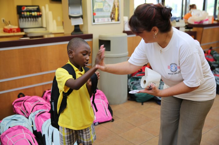 Jamie Rhodes, right, high-fives Khalil S. after handing him a backpack during Operation Homefront-Carolinas Back to School Brigade at Marine Corps Air Station Cherry Point, N.C., Aug. 15, 2014. School age children in grades ranging from pre-kindergarten to 12th grade received backpacks at the event. Rhodes is the family readiness officer with Marine Tactical Air Command Squadron 28. Khalil is a military dependent at Cherry Point. 