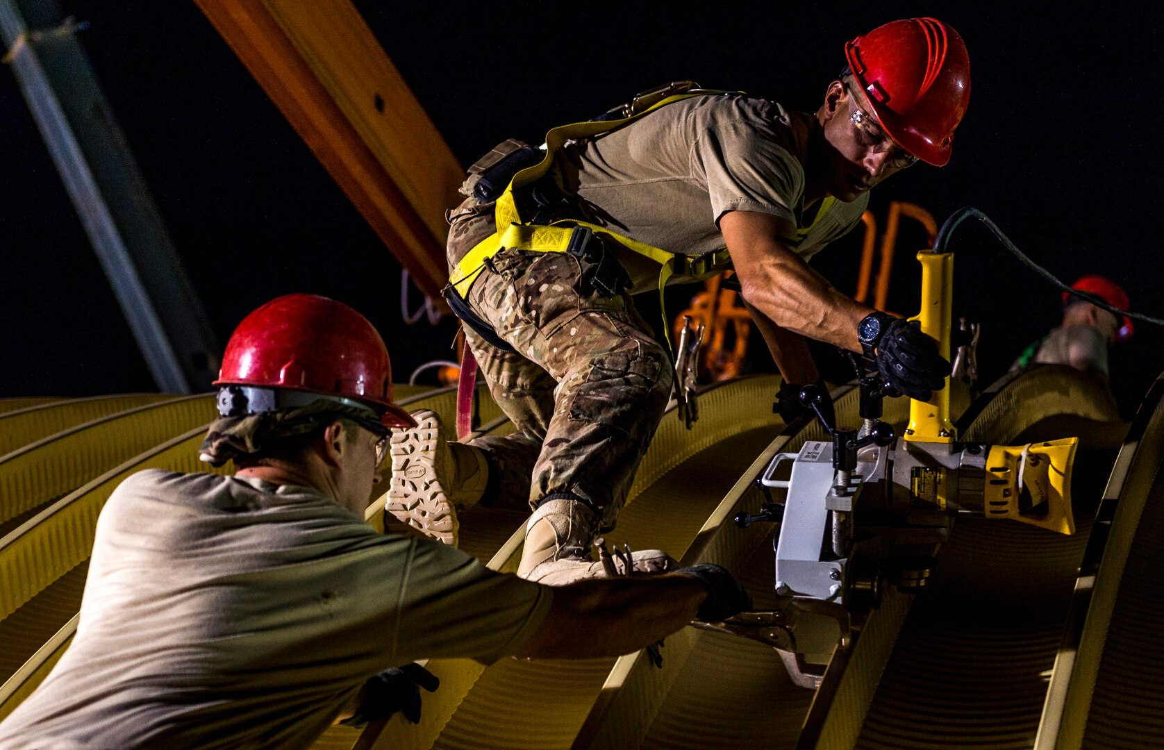 Senior Airman Nathan Hagy, 557th Expeditionary RED HORSE Squadron water fuels systems maintenance journeyman, passes a hand seamer to Staff Sgt. Nicholas Mundorff, 557th ERHS, while binding two steel arches together Aug. 4, 2014, at an undisclosed location in Southwest Asia. 