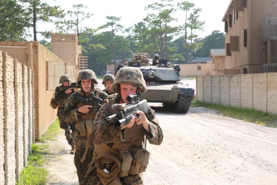 Marines with 1st Battalion, 24th Marine Regiment, move down a road while the street is covered by an M1A1 Abrams tank during an assault on a simulated enemy town Aug. 17, 2014, aboard Camp Lejeune, N.C., during exercise Heavy Metal 14. As the assault continued, instructors and safety personnel would point out a Marine to play the role of a wounded casualty to assess the team’s casualty evacuation performance.