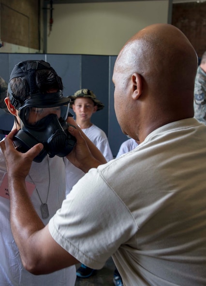 Tech. Sgt. Keith Thompson, 442nd Logistics Readiness Squadron material management technician, assists a Joint Base Pearl Harbor-Hickam youth with trying on a gas mask in Bldg. 2115 at JBPHH, Hawaii, Aug. 15, 2014, during Operation Hele On, a mock deployment line intended to help children understand the process parents go through before a deployment. More than 130 children attended the full day event which included an intelligence briefing, mobility bag pickup, obstacle course, drill competition, combat arms training and a C-17 static tour. (U.S. Air Force photo by Tech. Sgt. Terri Paden)