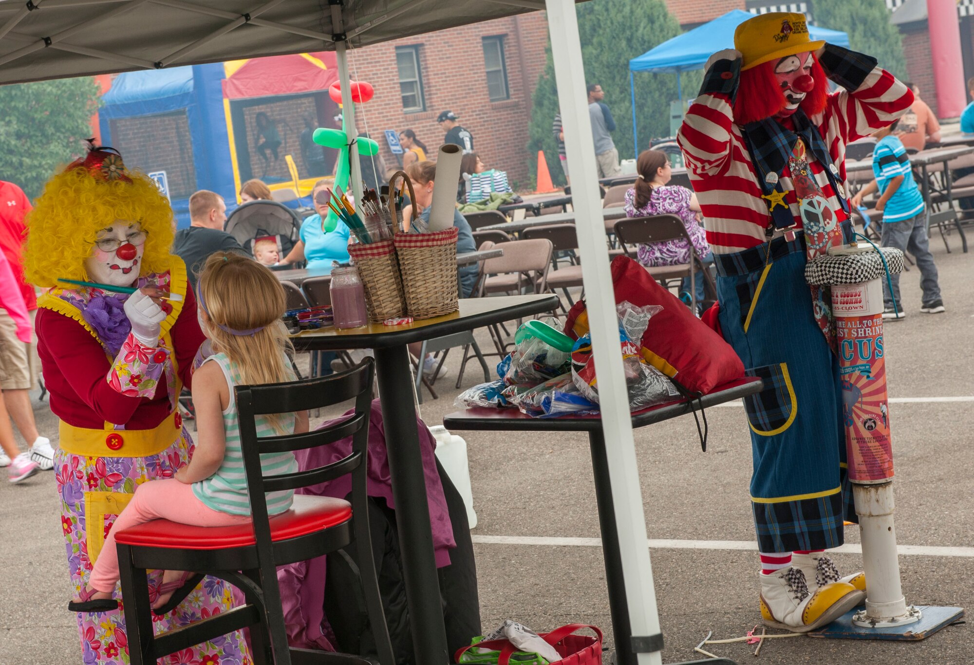A clown paints a child’s face, while the other blows up balloons during the Annual Summer Block Party on Minot Air Force Base, N.D., Aug. 16, 2014. The event featured a burger burn, inflatables, and the Show and Shine Car Show. (U.S. Air Force photo/Airman 1st Class Apryl Hall)