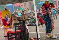 A clown paints a child’s face, while the other blows up balloons during the Annual Summer Block Party on Minot Air Force Base, N.D., Aug. 16, 2014. The event featured a burger burn, inflatables, and the Show and Shine Car Show. (U.S. Air Force photo/Airman 1st Class Apryl Hall)