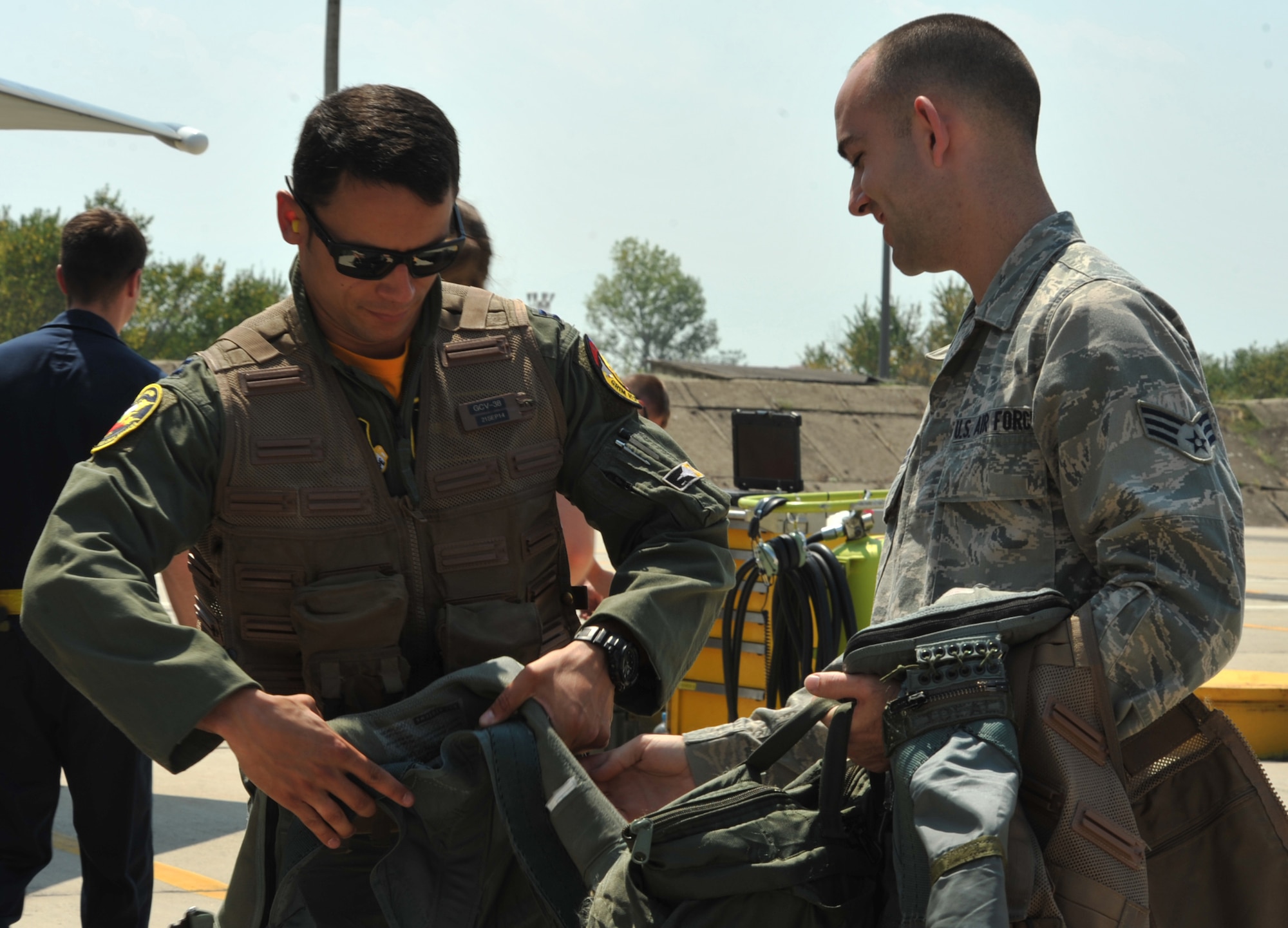 Senior Airman Jeffrey Berry (right), 493rd Fighter Squadron aircrew flight equipment technician, receives a harness and vest from a pilot after his flight Aug. 15, 2014. Aircrew flight equipment Airmen provide pilots with the life-saving equipment which allows them to fly. (U.S. Air Force photo/Senior Airman Hailey Haux)