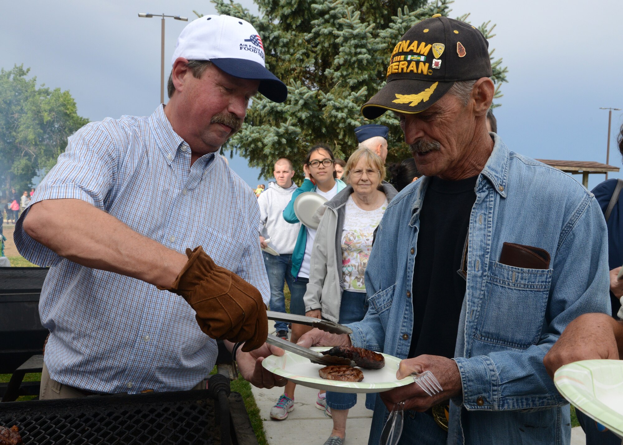 Chris Jones, Steak Team Mission member (left), serves food to David Paddock, a Vietnam veteran, during a steak dinner Aug. 15 at Sun Plaza Park at Malmstrom Air Force Base, Mont. Steak Team Mission, a nonprofit organization that provide food for U.S. service members, provided 1,200 steaks for Airmen and their families and retirees. (U.S. Air Force photo/Senior Airman Katrina Heikkinen)