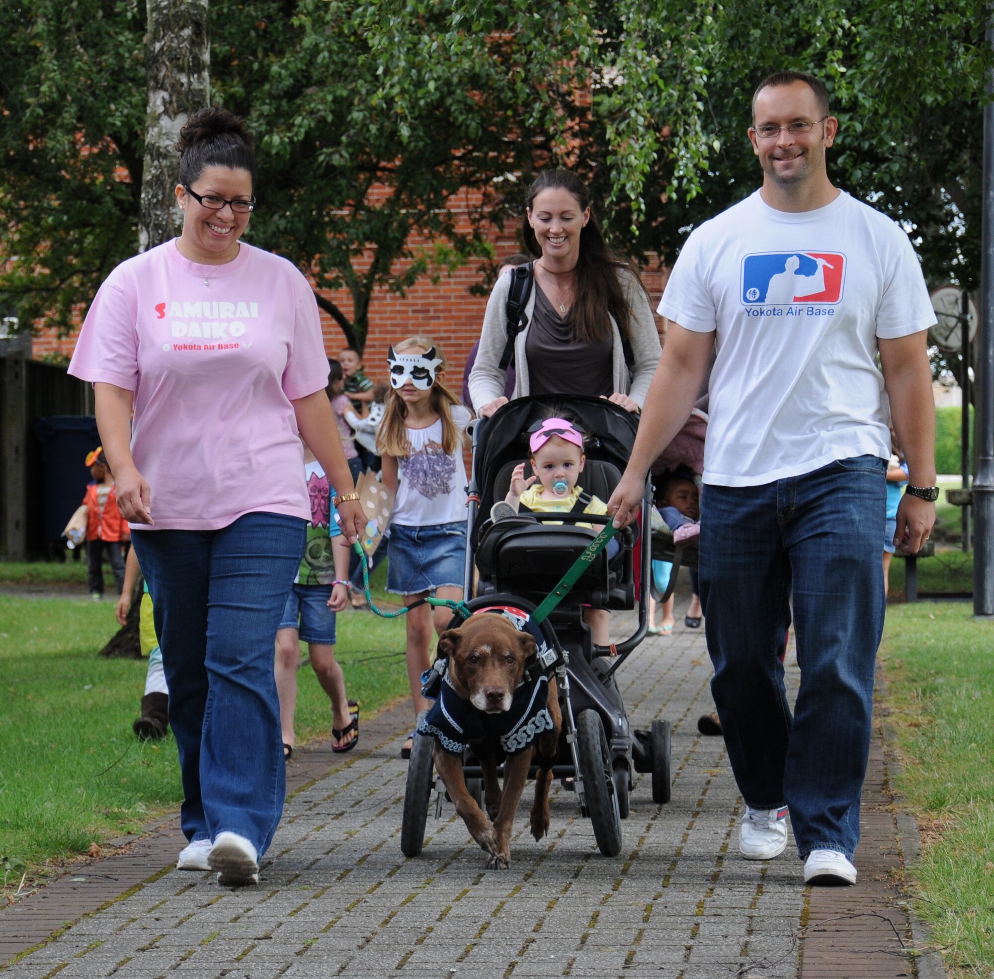 U.S. Air Force Master Sgt. Christopher Gerwick, right, 100th Civil Engineer Squadron Fire Department assistant chief of operations from Eaglewood, Ohio, and his wife Shannon, left, lead their dog Reece during a “Paws to Read” pet parade and costume contest Aug. 13, 2014, at the library on RAF Mildenhall, England. Organizers encouraged guests to bring a real pet or a stuffed animal for the parade. (U.S. Air Force photo/Gina Randall/Released)